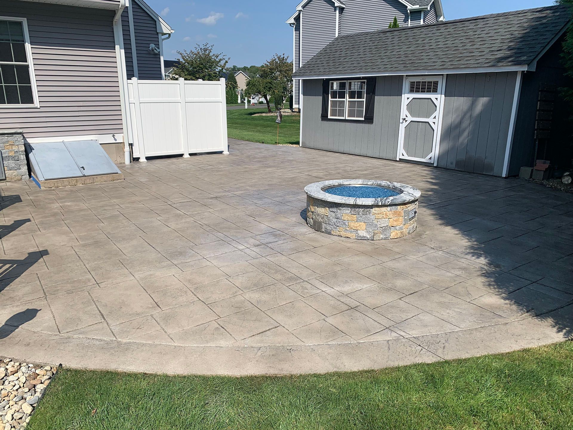 Backyard patio with stamped concrete, fire pit, and small gray shed beside two houses