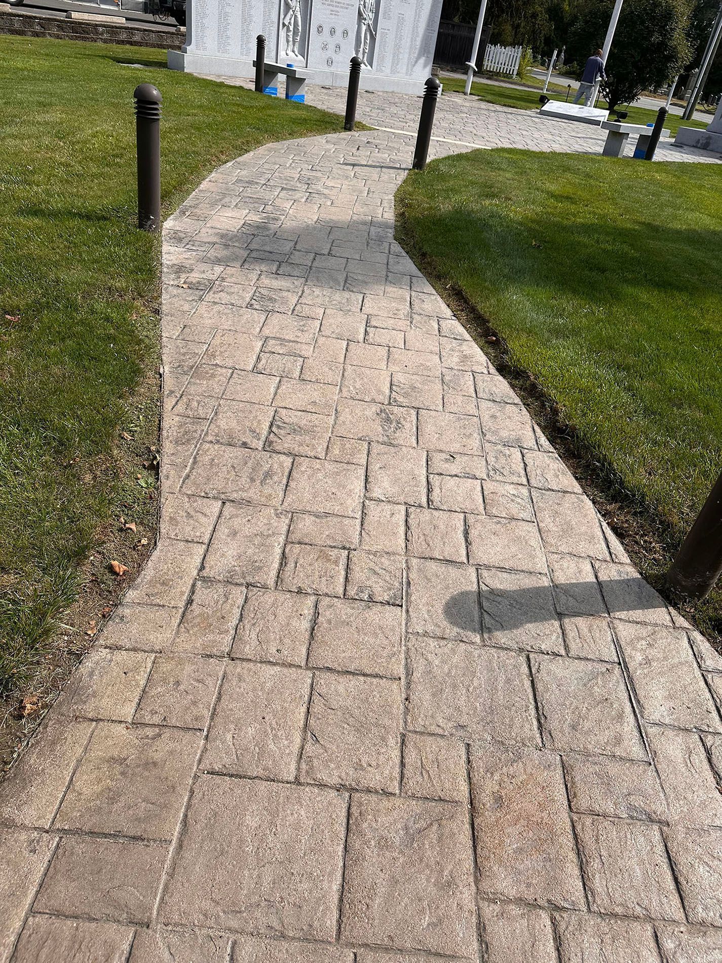Curved brick walkway through grass toward a building entrance, with black posts lining the path.