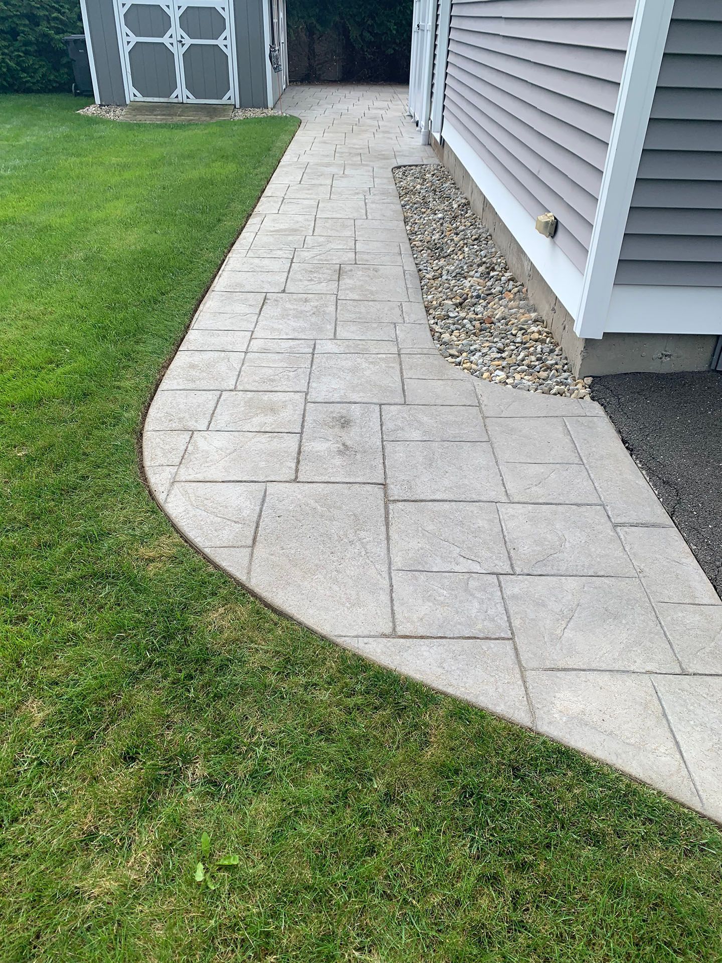 Curved stone walkway along a house beside green lawn and gravel border