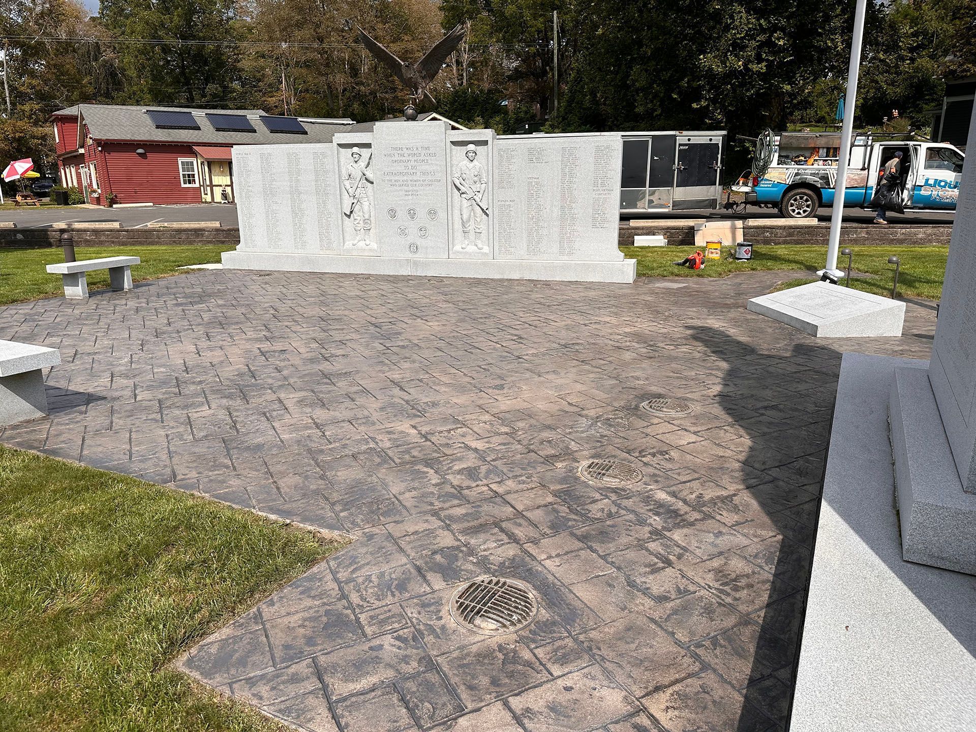 Memorial plaza with white stone wall, brick paving, and benches in a park setting