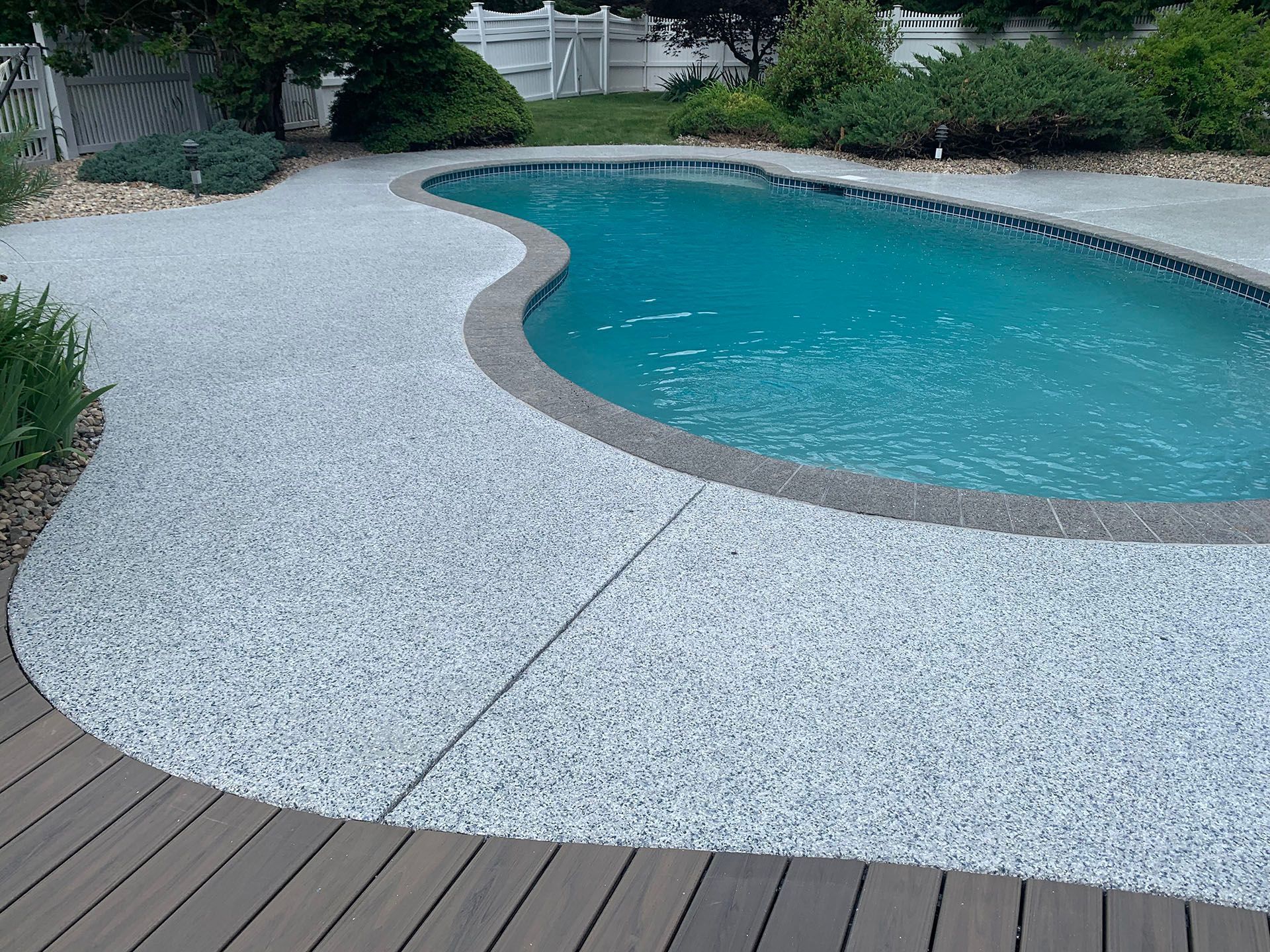 Curved backyard swimming pool with turquoise water and white gravel patio
