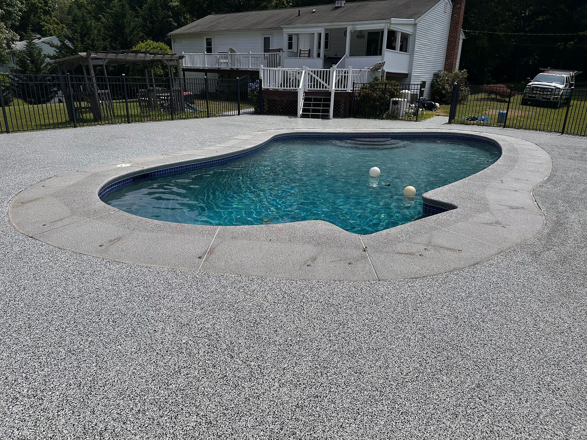 Backyard swimming pool with turquoise water, surrounded by a light stone deck and a white house in the background