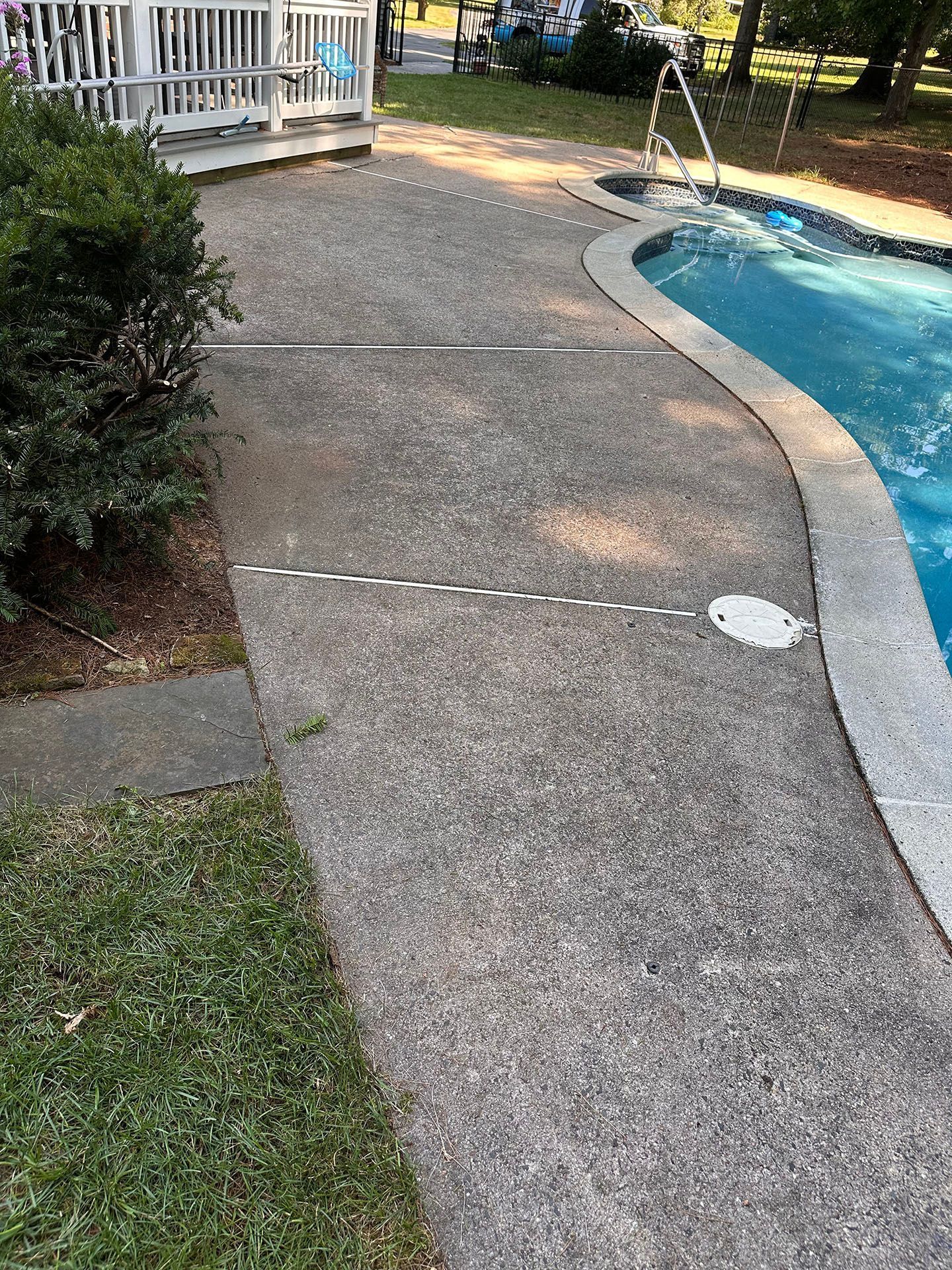 Curved concrete pool deck beside blue water, with white railing and grass border.