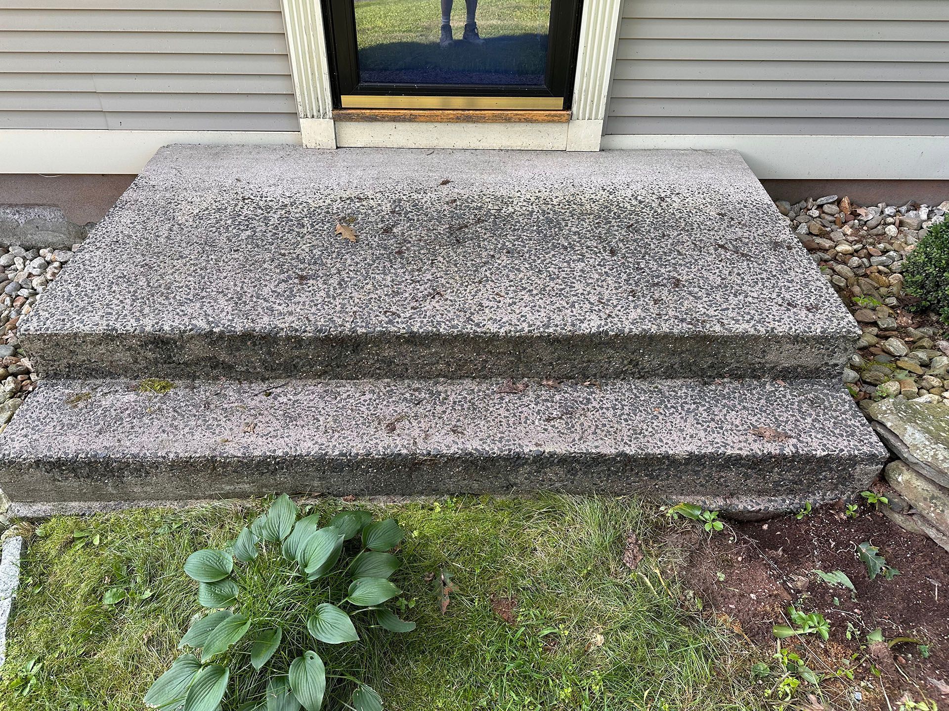 Concrete front steps leading to a house entryway, with a small patch of grass and plants below.