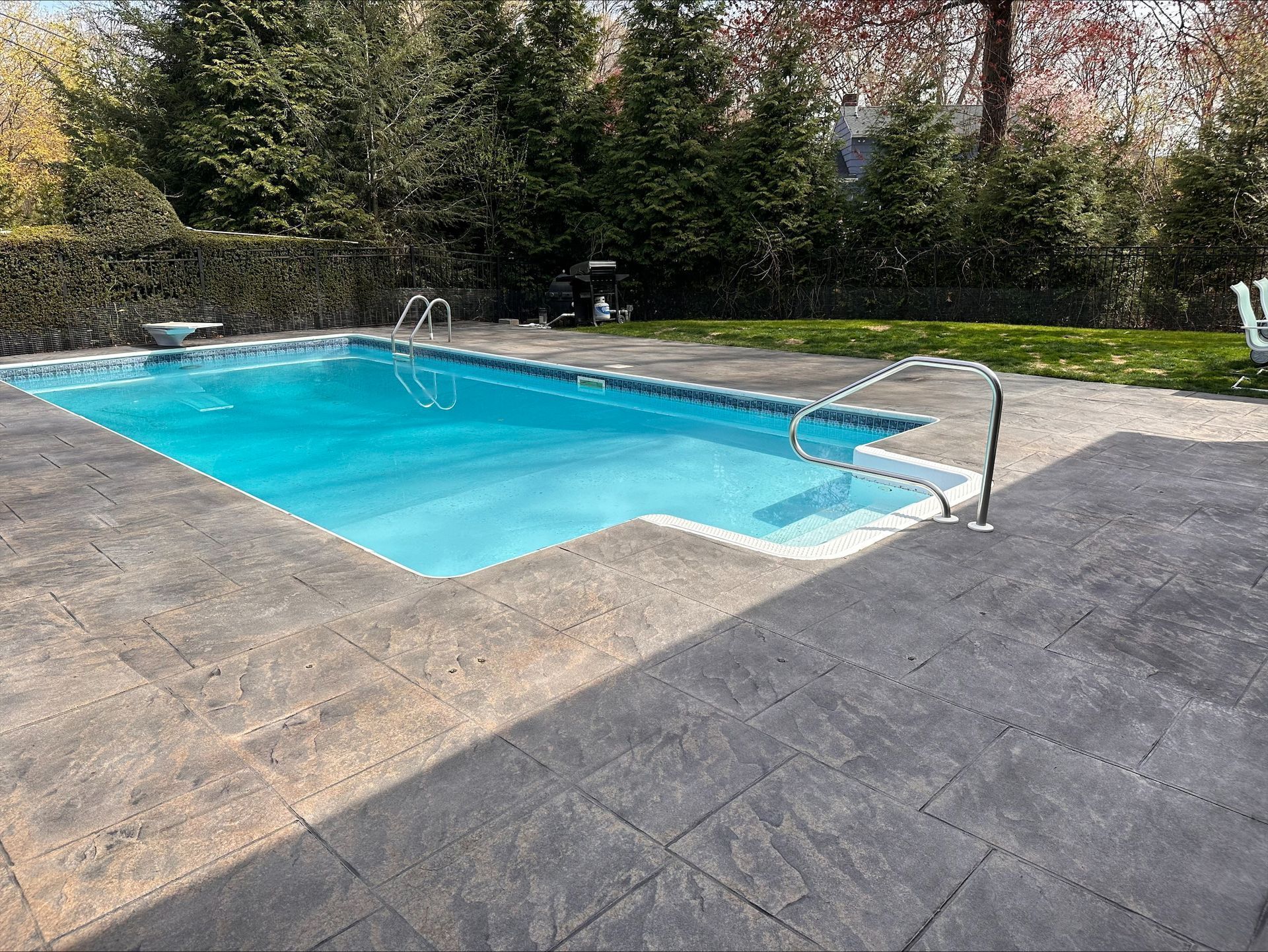 Backyard swimming pool with turquoise water, gray patio, and trees in the background