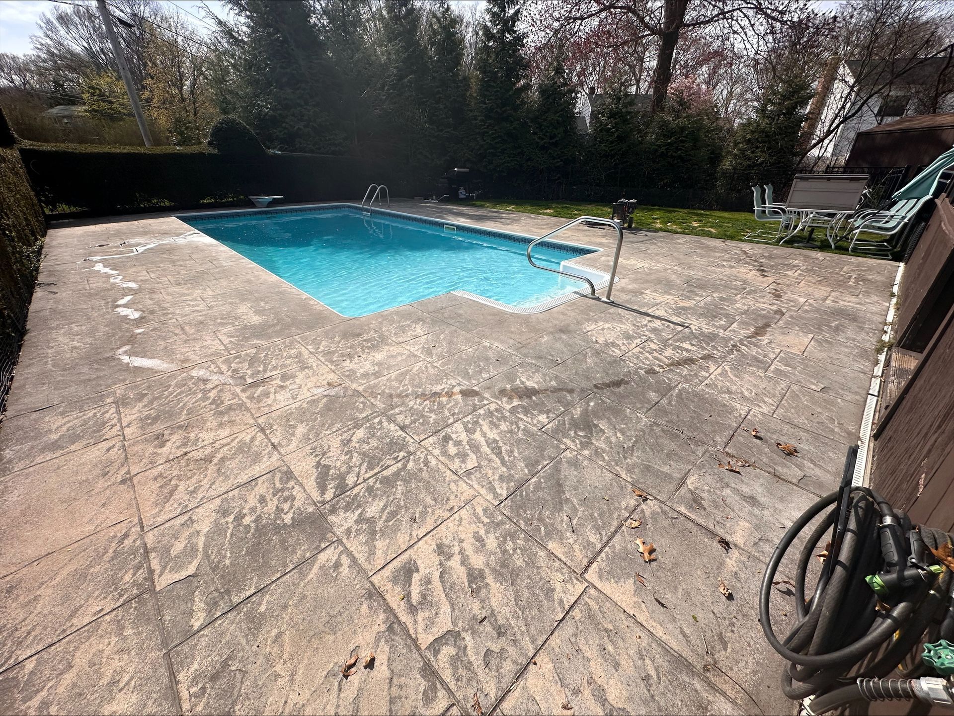 Backyard patio with a small blue swimming pool and trees in the background