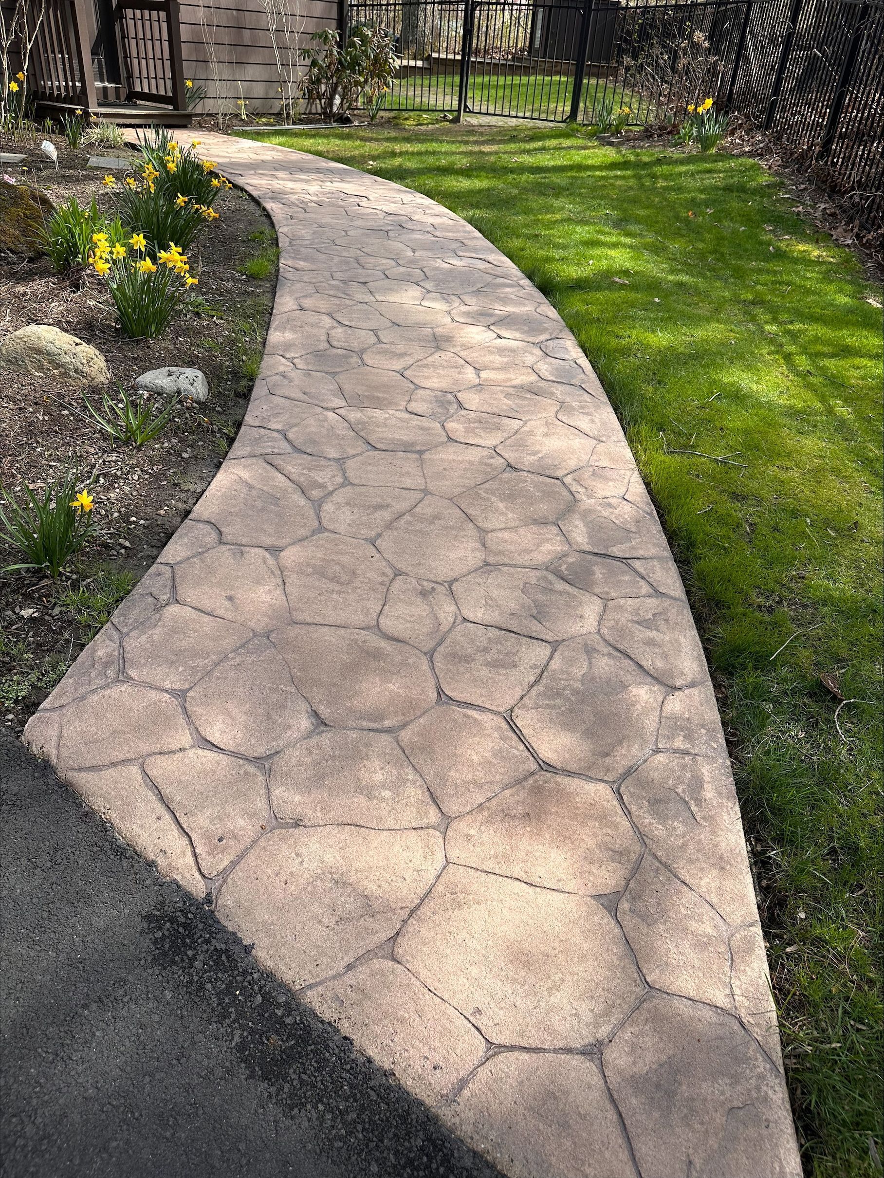 Curved stone garden walkway beside green lawn and flower bed in sunlight