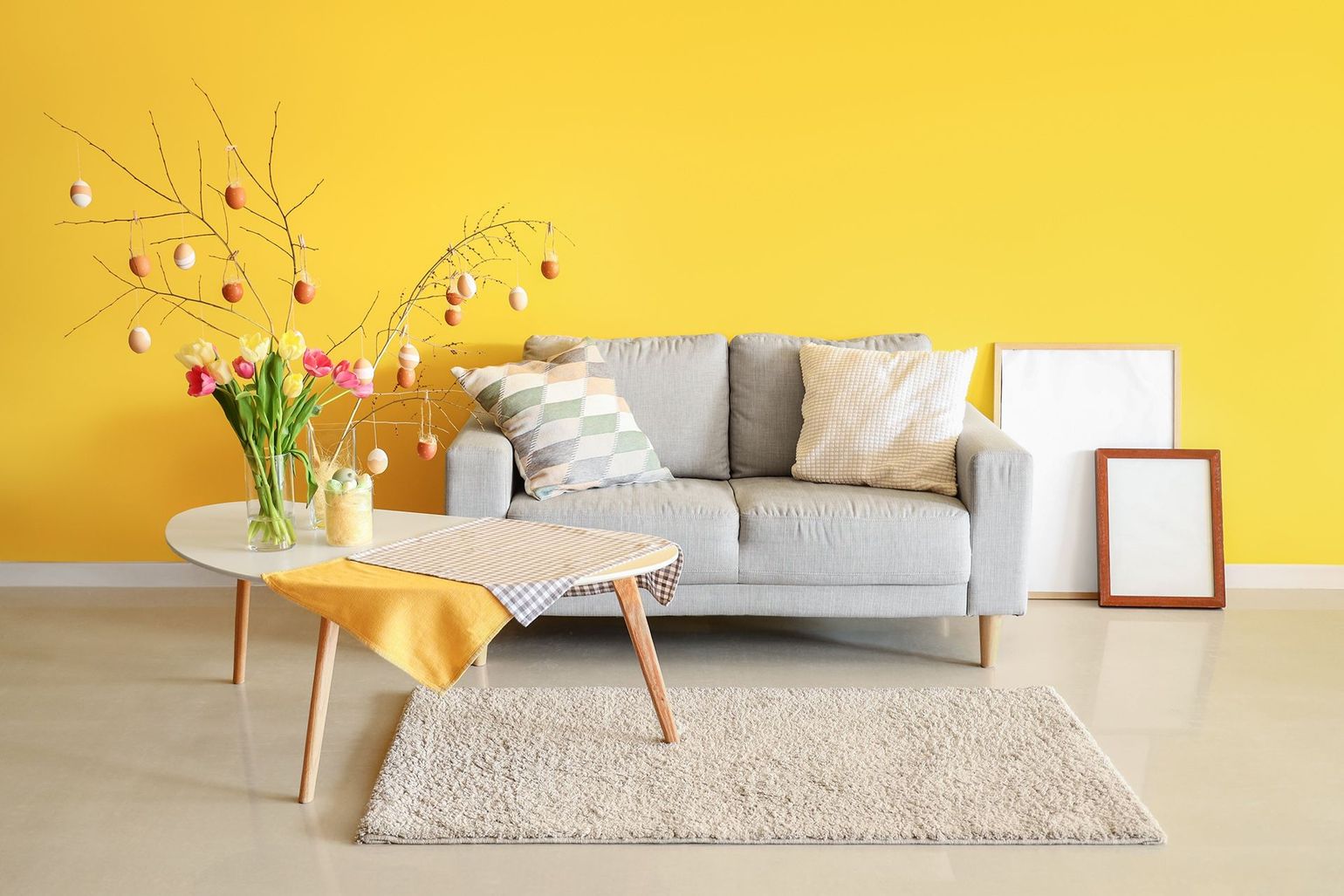 Modern living room with a gray sofa, yellow accent wall, coffee table, rug, and vase of flowers
