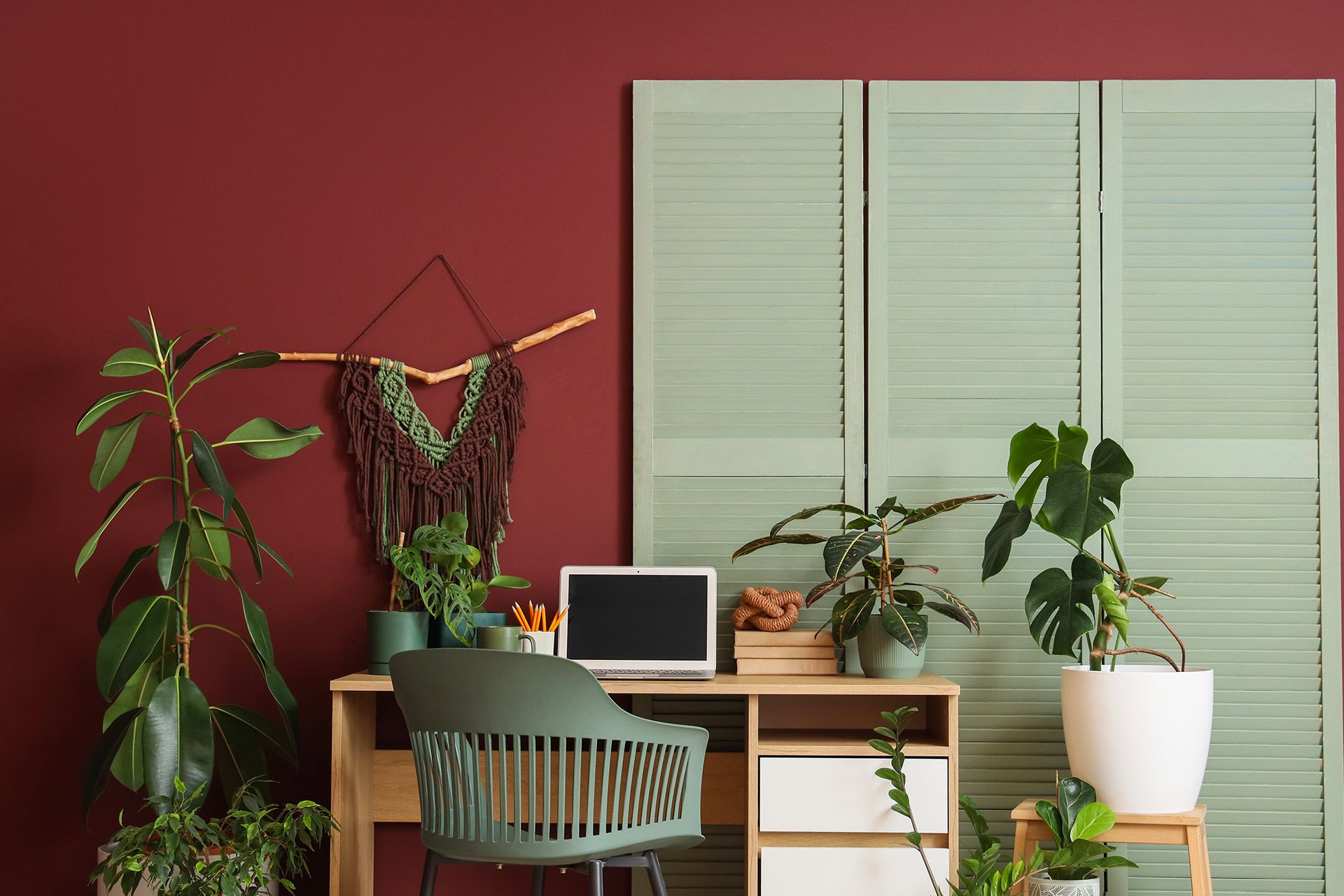 Cozy home office with laptop, desk, chair, and several potted plants against a red wall