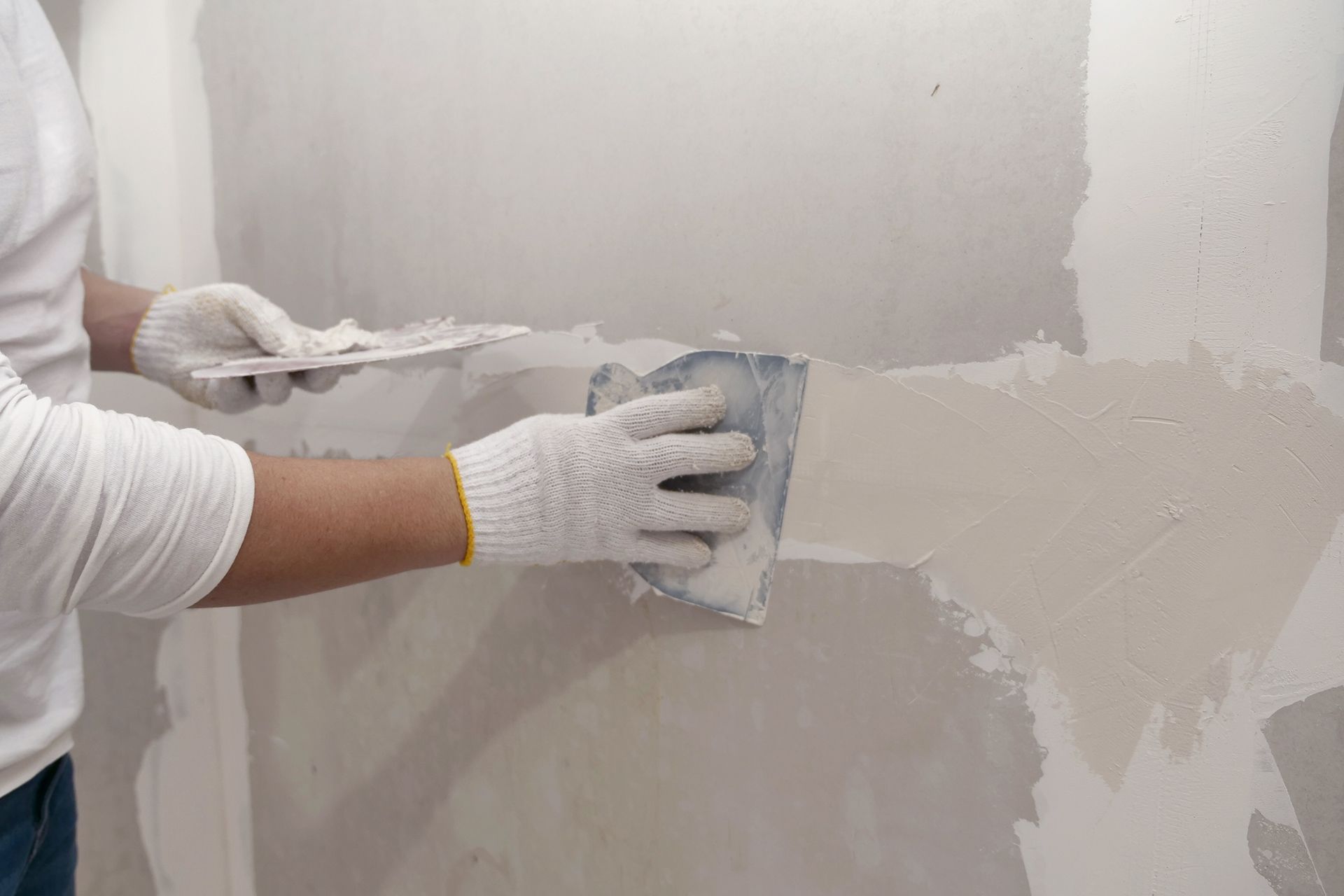 Hands using a putty knife to smooth gray drywall compound on a wall