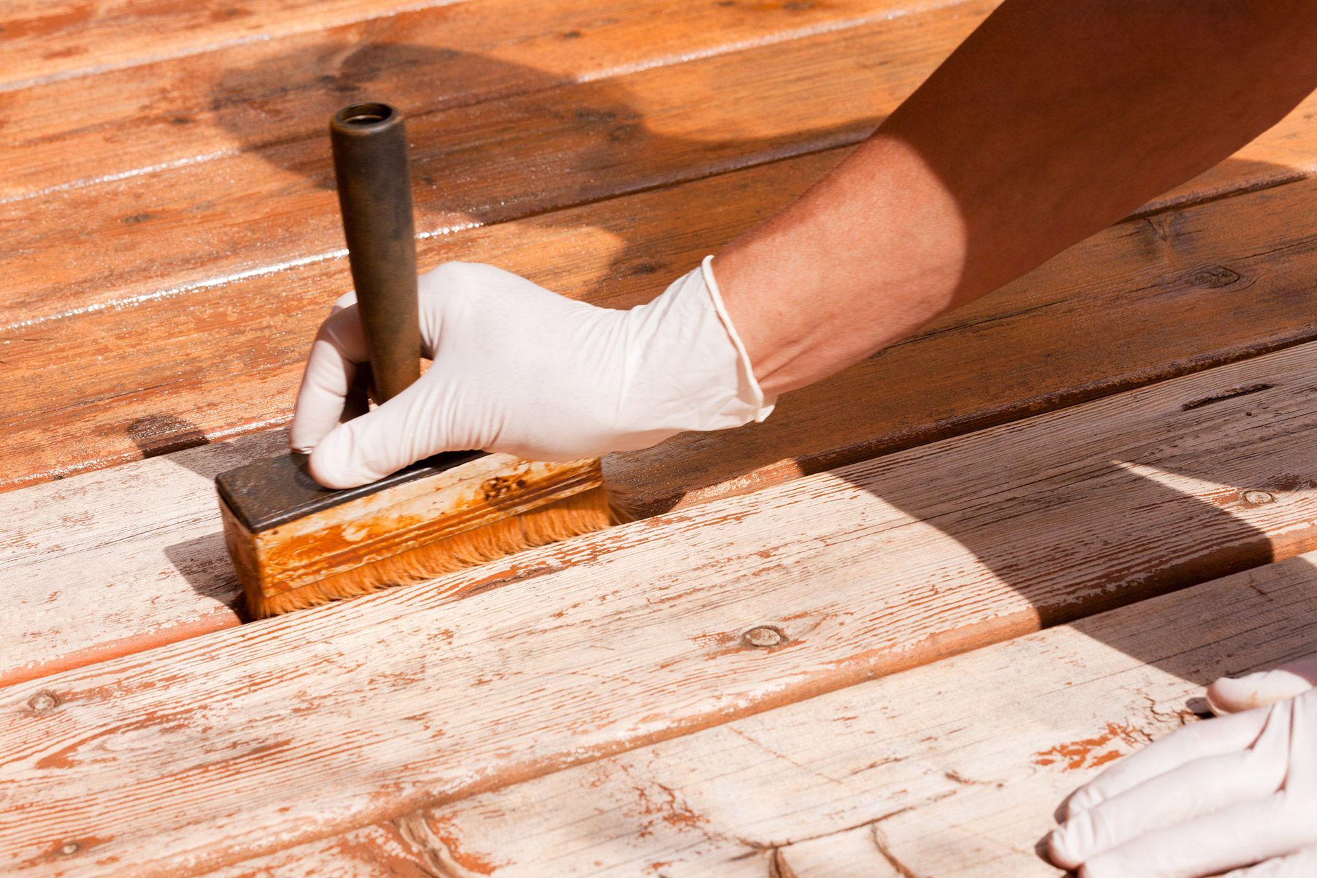 Gloved hand applying stain to a wooden deck with a brush