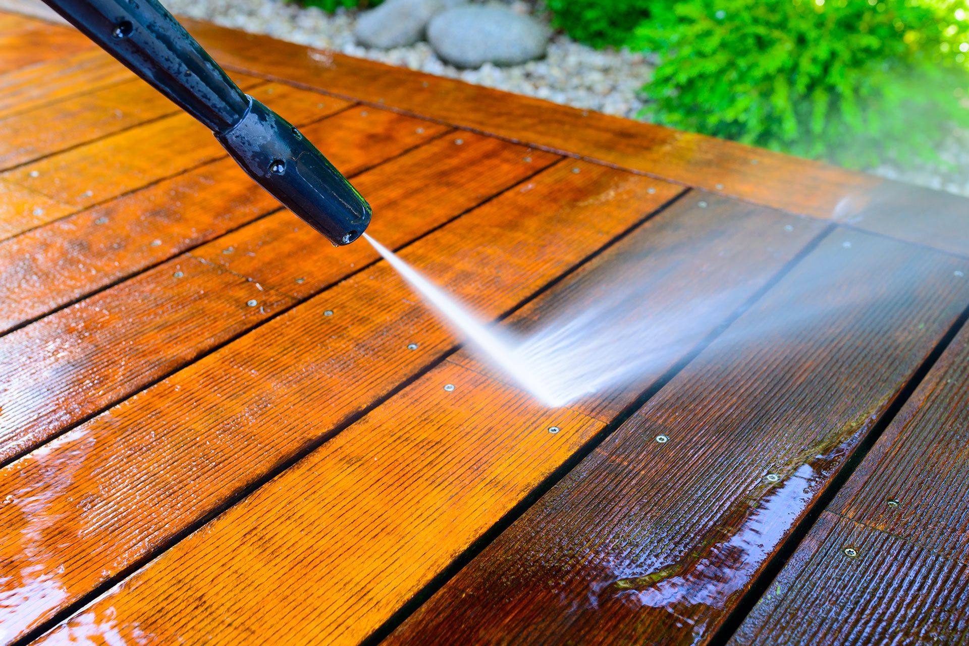 Pressure washing a wet wooden deck with a high-powered spray nozzle