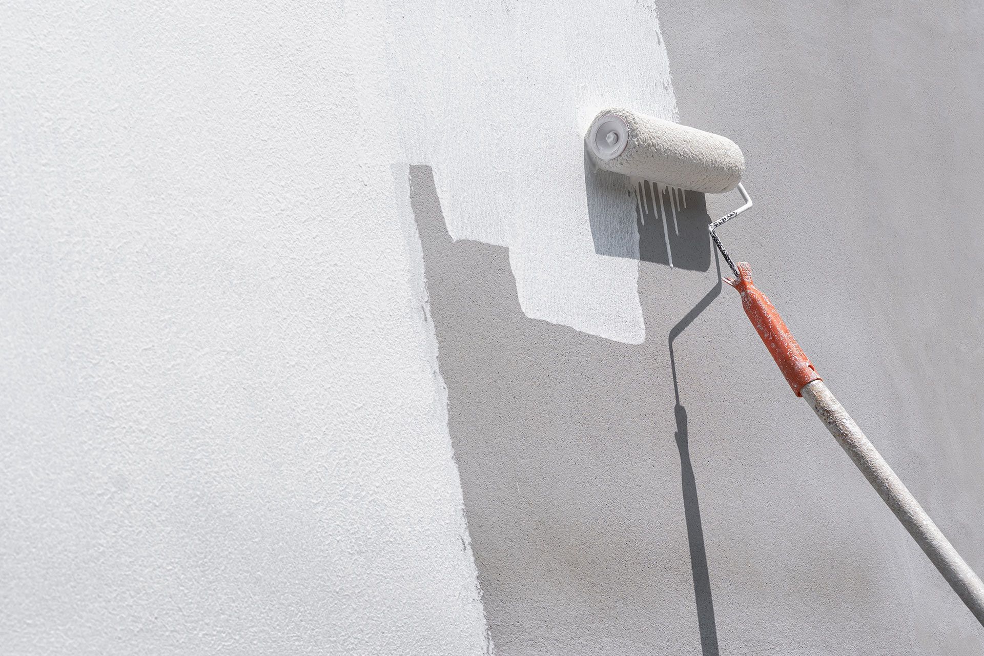 Paint roller applying white paint to a wall, leaving a wet patch and shadow.