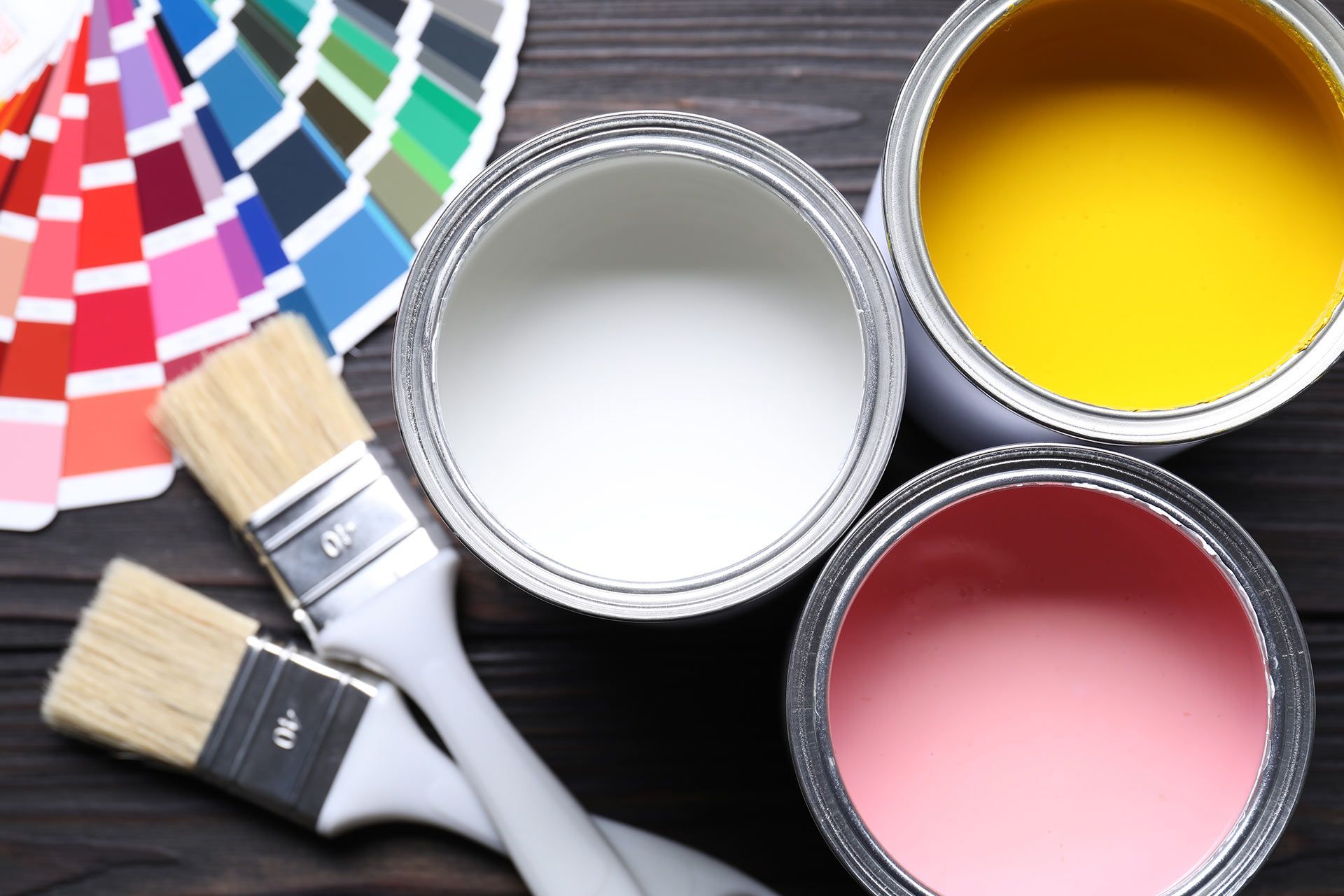 Paint cans and brushes beside a fan of color swatches on a dark surface