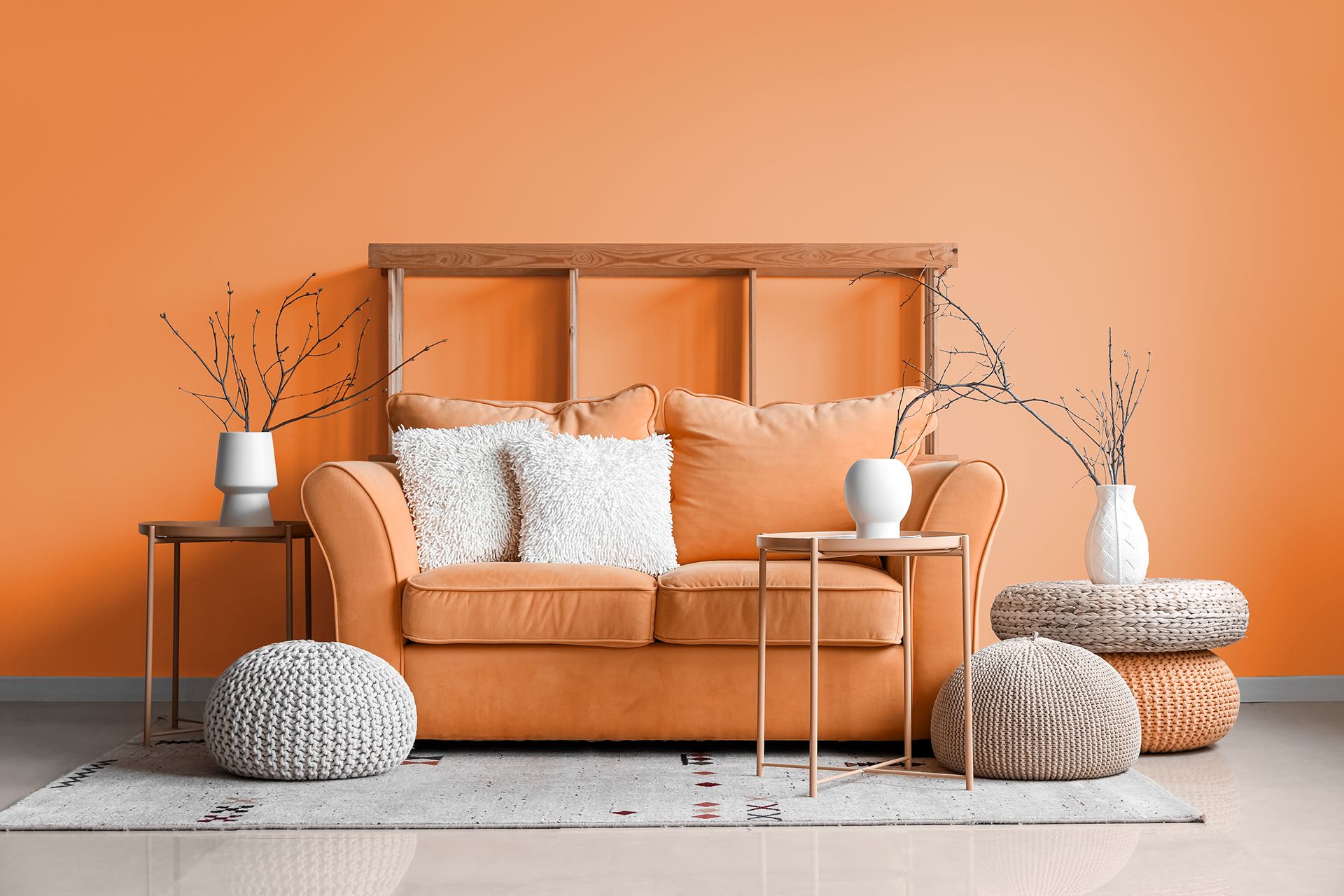 Orange sofa in a cozy modern living room with neutral pillows, side tables, and dried branches against an orange wall