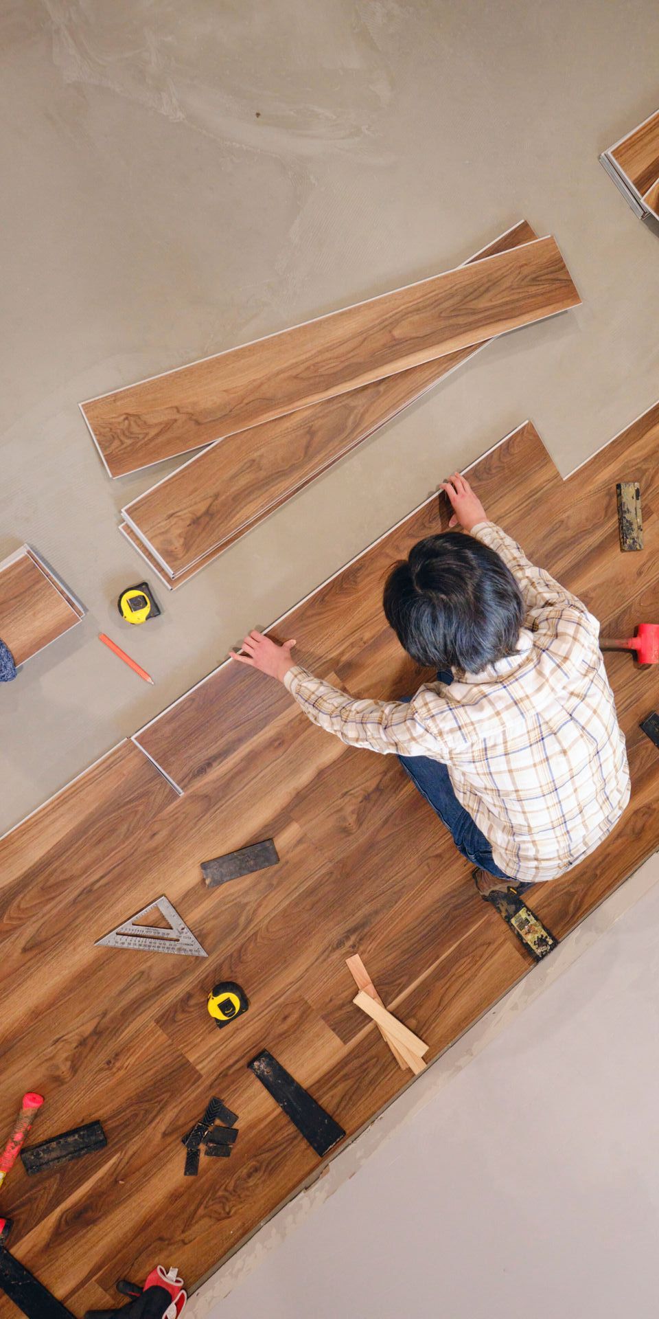 A man is sitting on the floor installing a wooden floor.