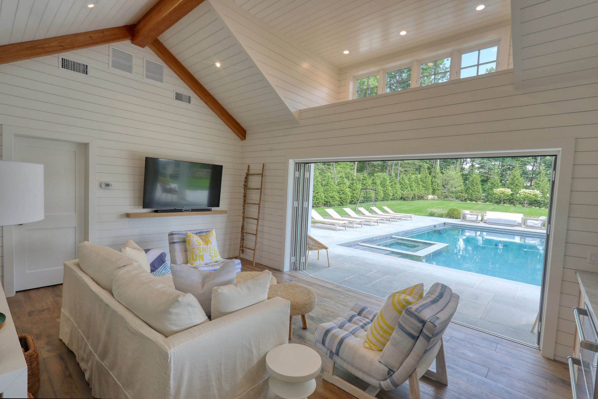 A living room with a couch , chairs , television and a swimming pool.