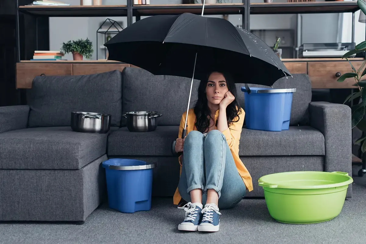 A woman is sitting on the floor under an umbrella in a living room.