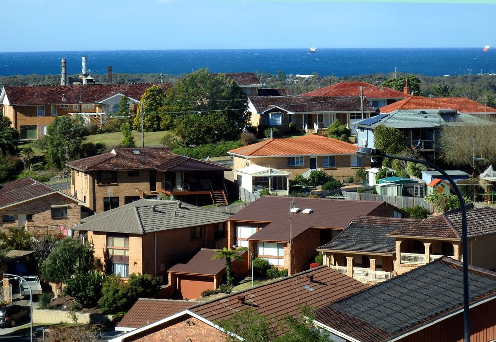 Houses with red, brown, and gray roofs overlook the blue ocean and sky.