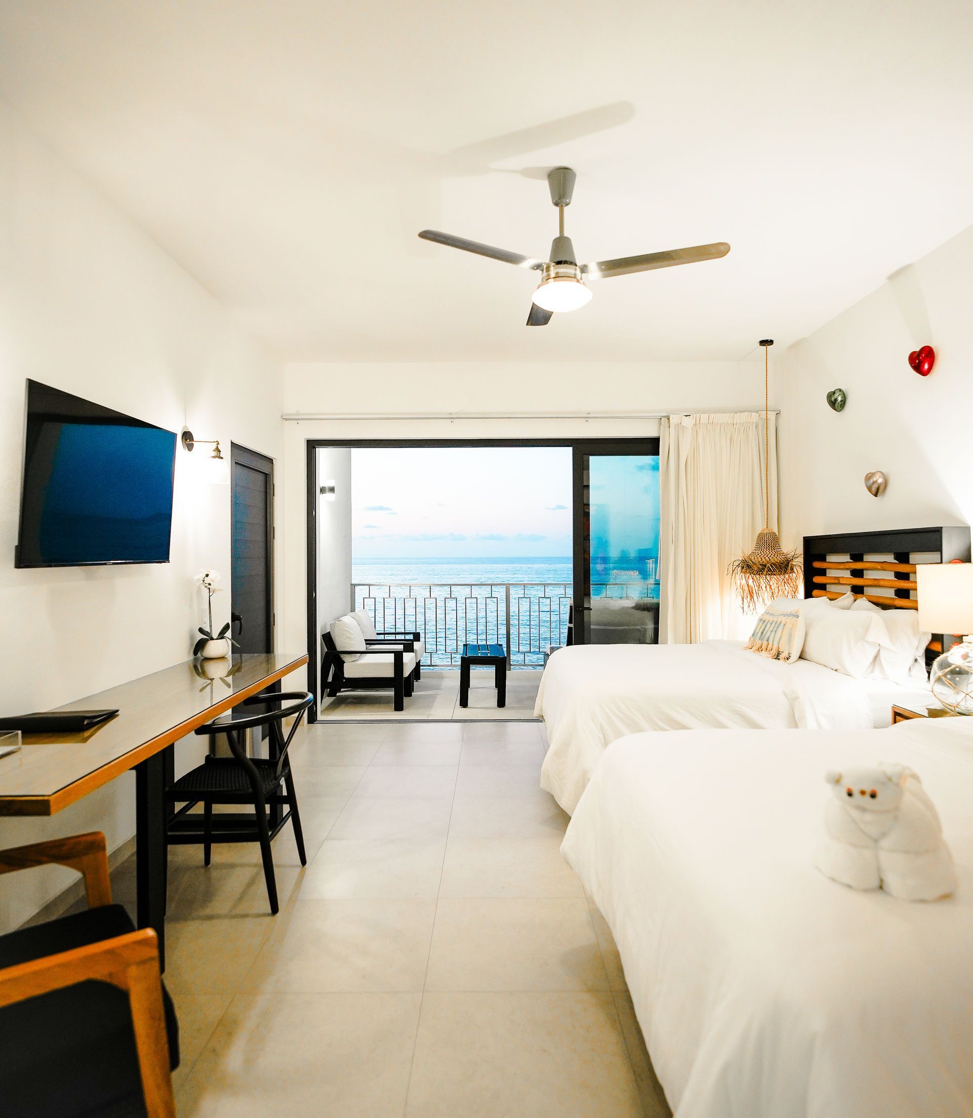 Bright hotel room with twin beds, TV, desk, and balcony ocean view