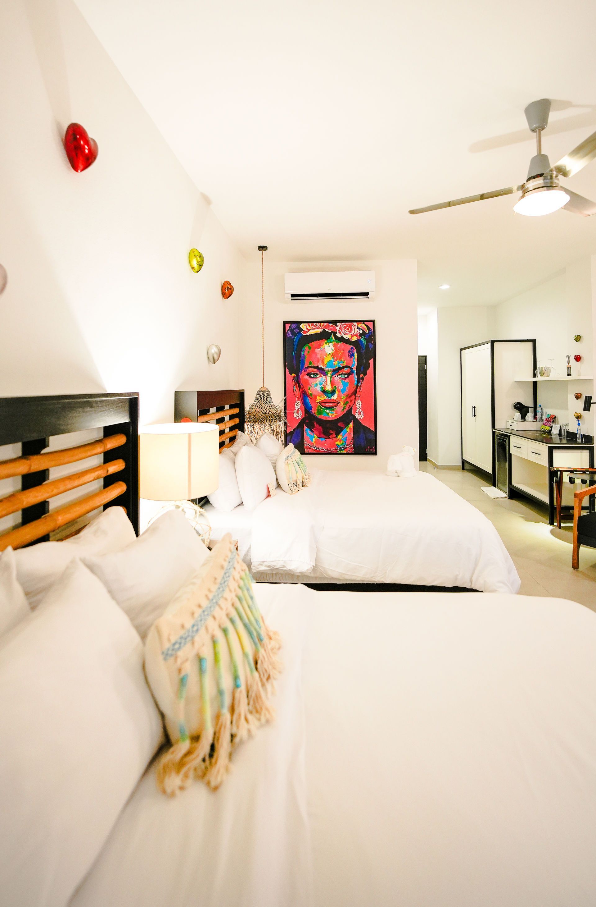 Bright white bedroom with a bed, ceiling fan, colorful wall art, and mirrored closet doors