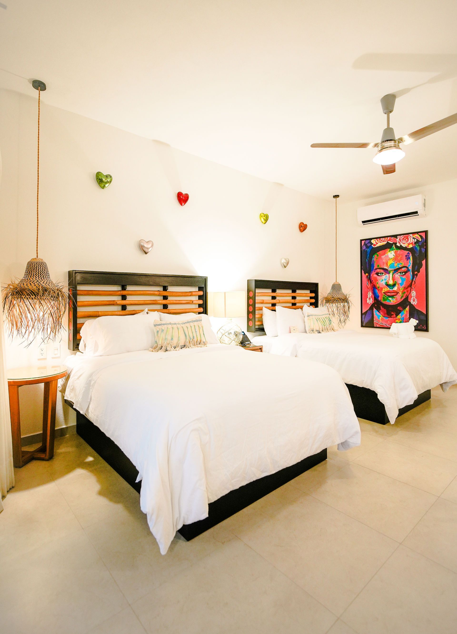 Bright bedroom with two white beds, heart wall decor, and colorful art on the wall.