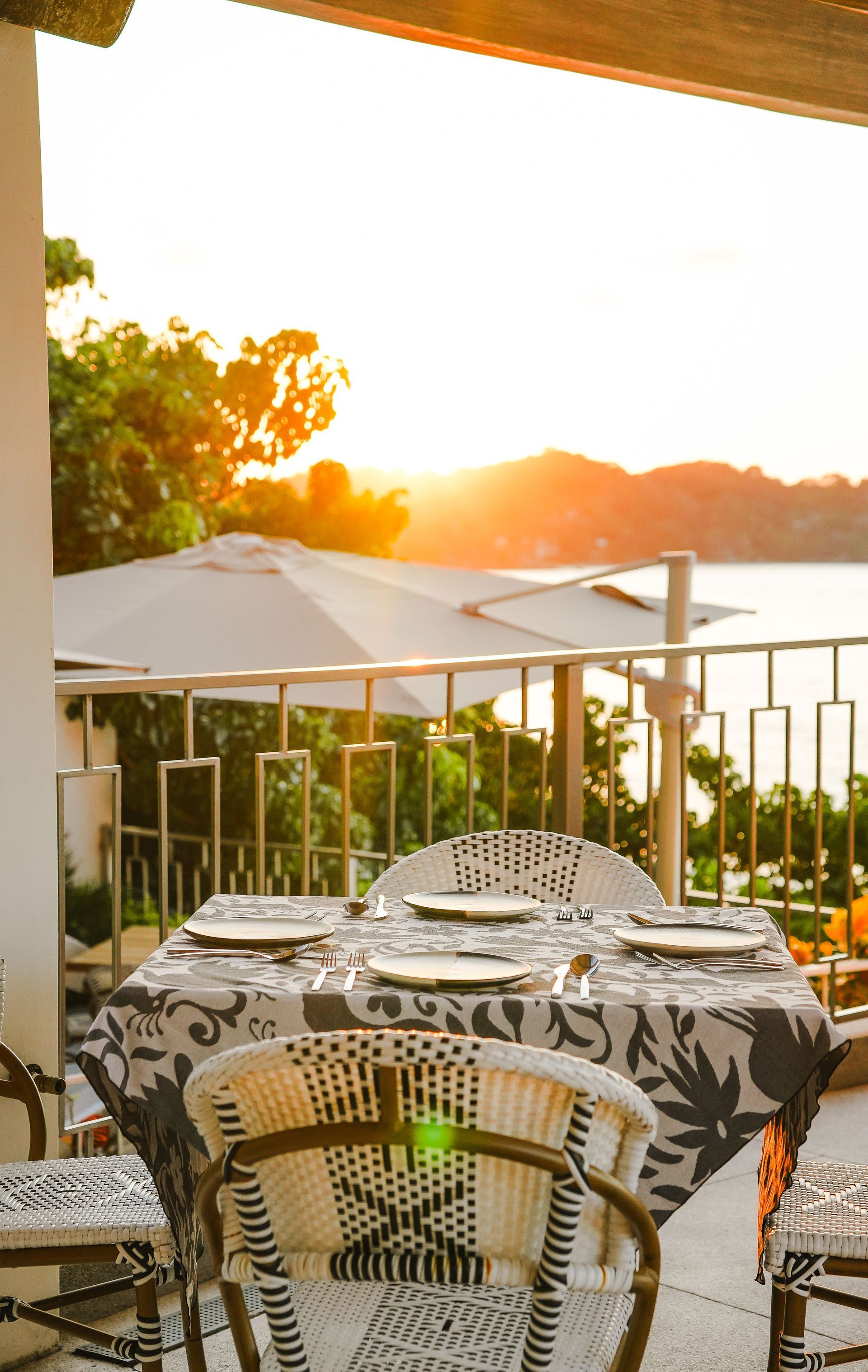 Sunlit outdoor café table with patterned chairs overlooking a railing and trees at sunset