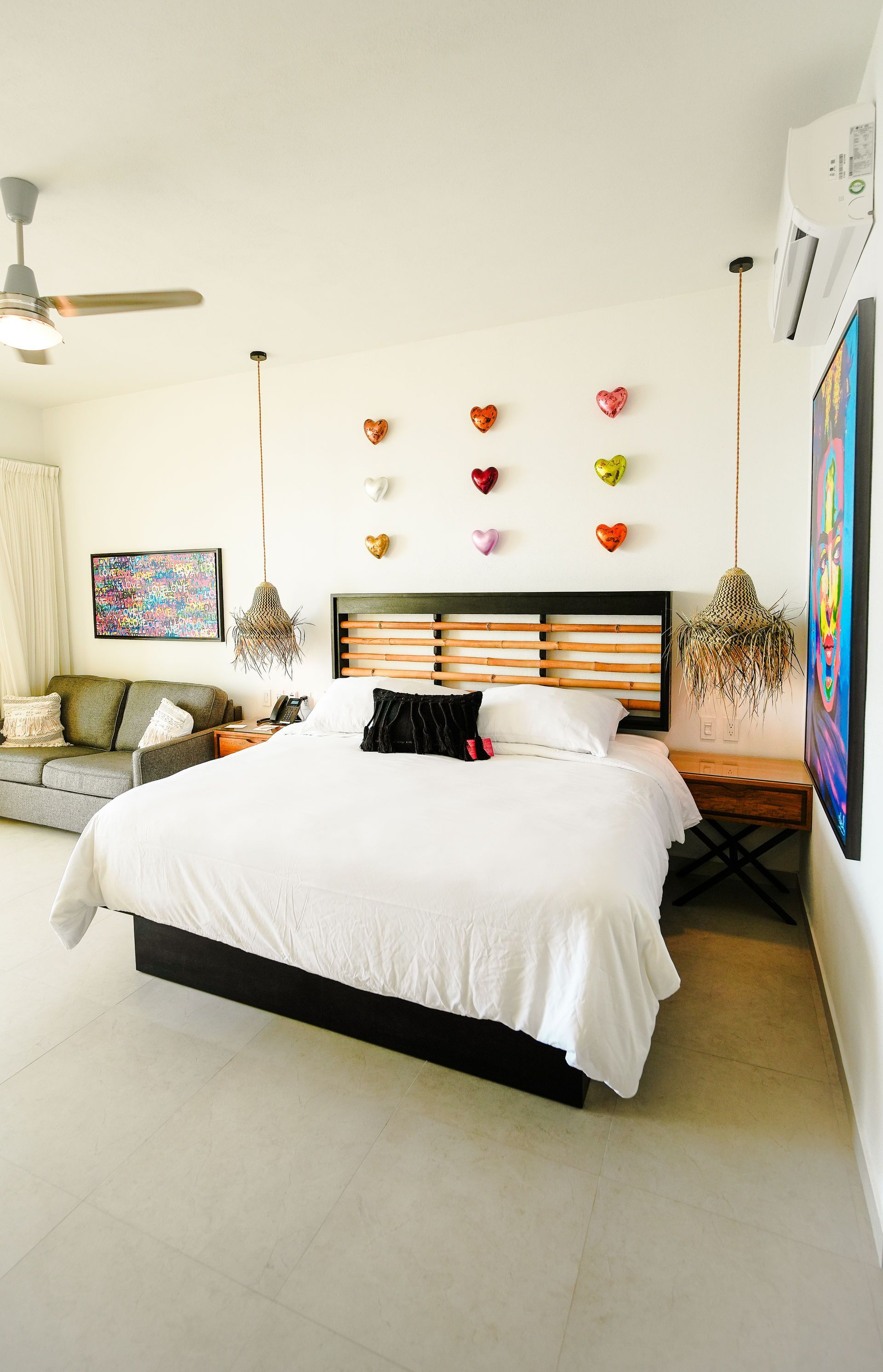 Bright bedroom with a white bed, colorful wall decor, ceiling fan, and large art on the wall
