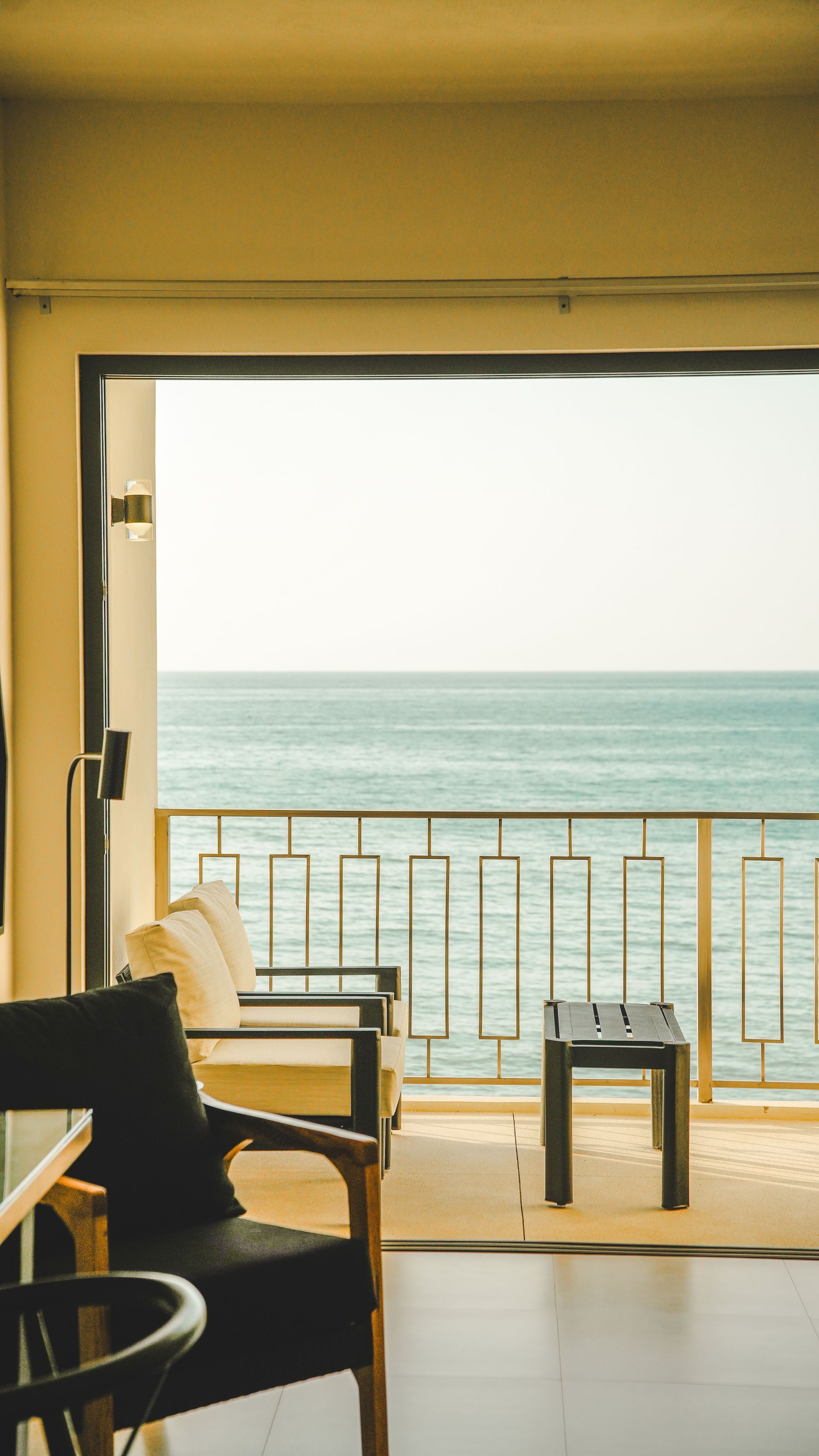 Seaside patio with chairs and table overlooking a calm blue ocean through a large opening.