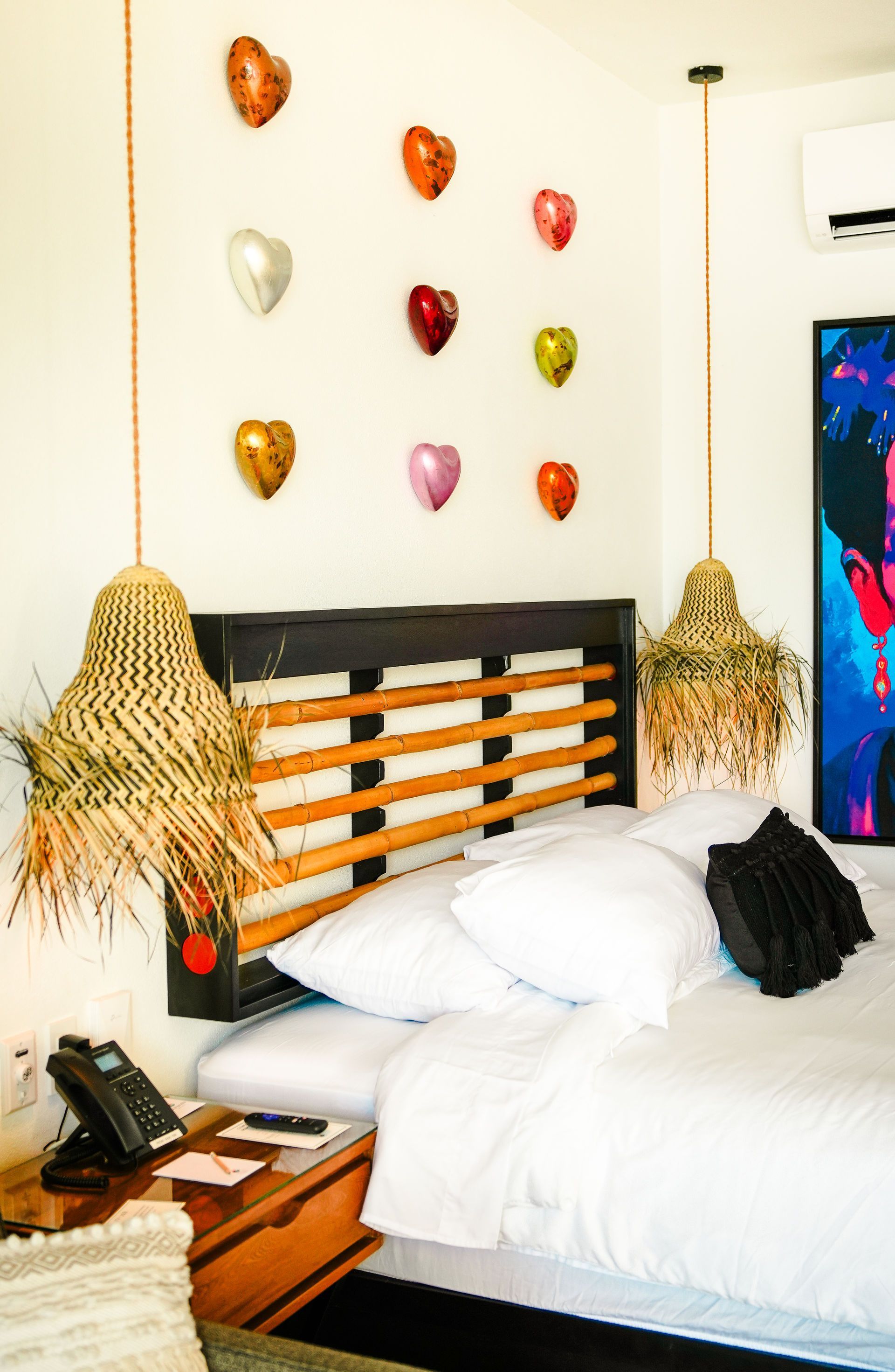 Cozy bedroom with white bedding, wooden headboard, woven pendant lights, and colorful heart wall art