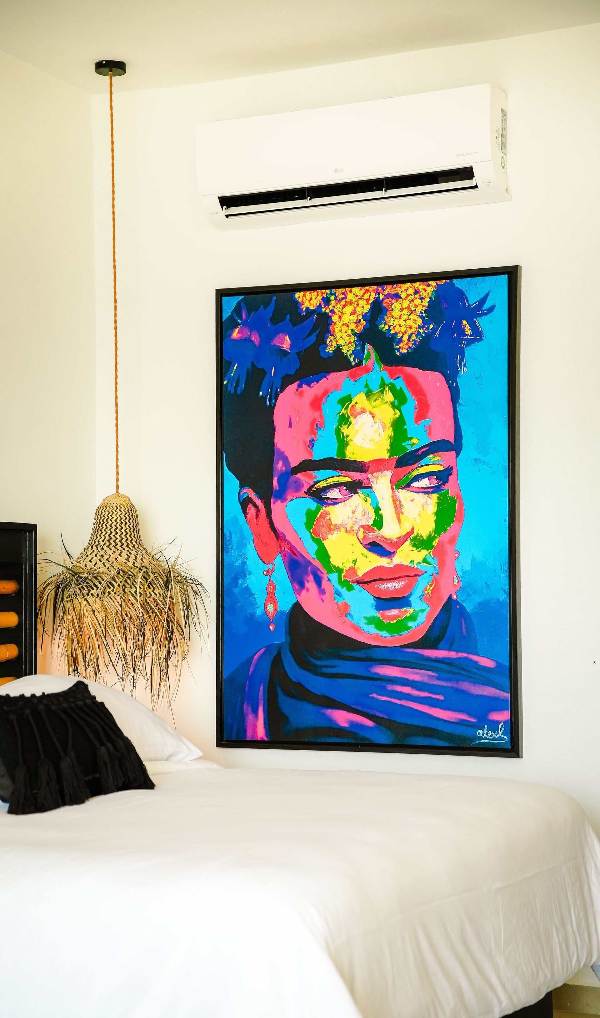 Colorful pop-art portrait above a bed in a bright bedroom with a hanging plant and wall-mounted AC