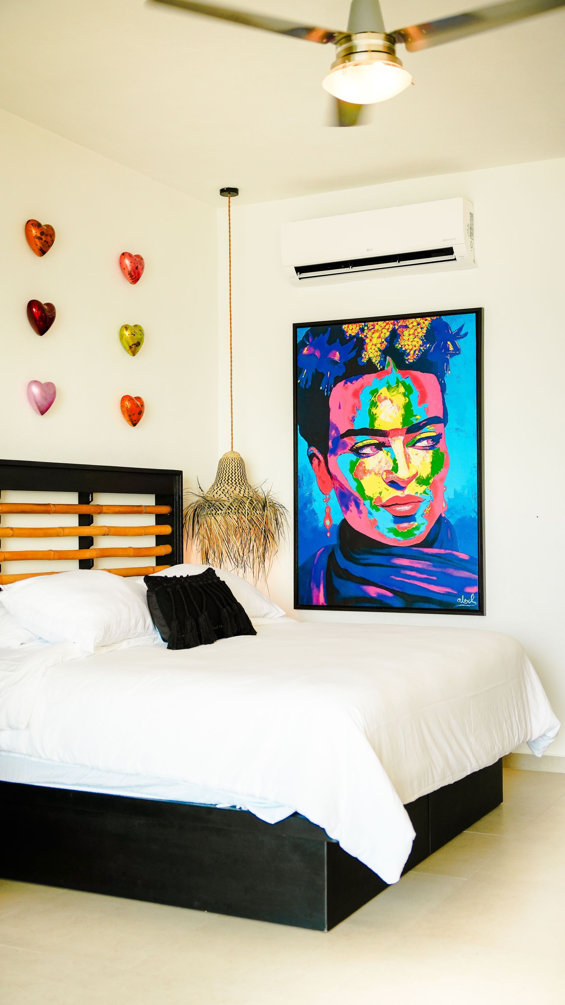 Bright bedroom with a white bed, colorful portrait wall art, heart decorations, and a ceiling fan