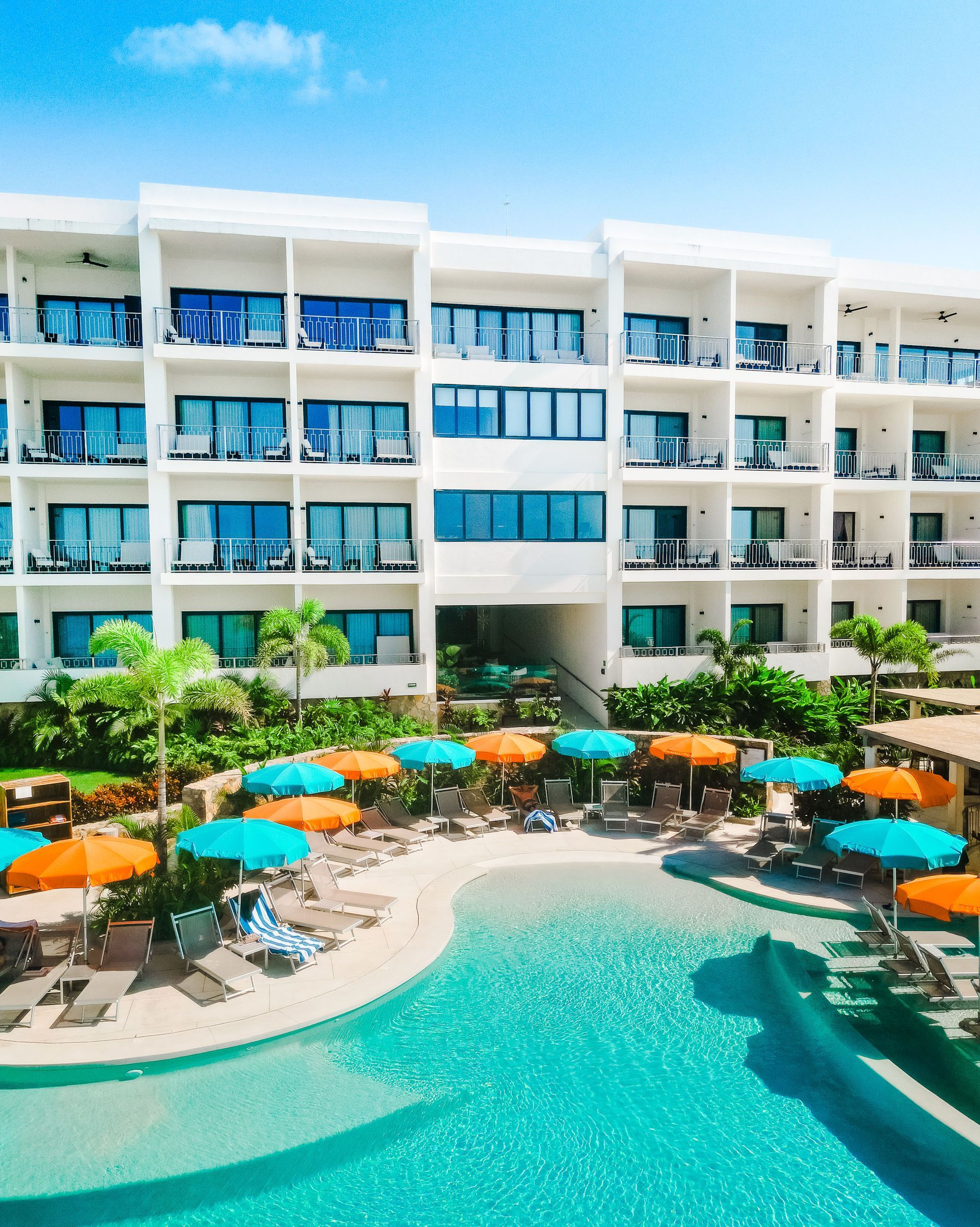 Modern resort hotel with turquoise pool, orange umbrellas, and balconies overlooking the courtyard