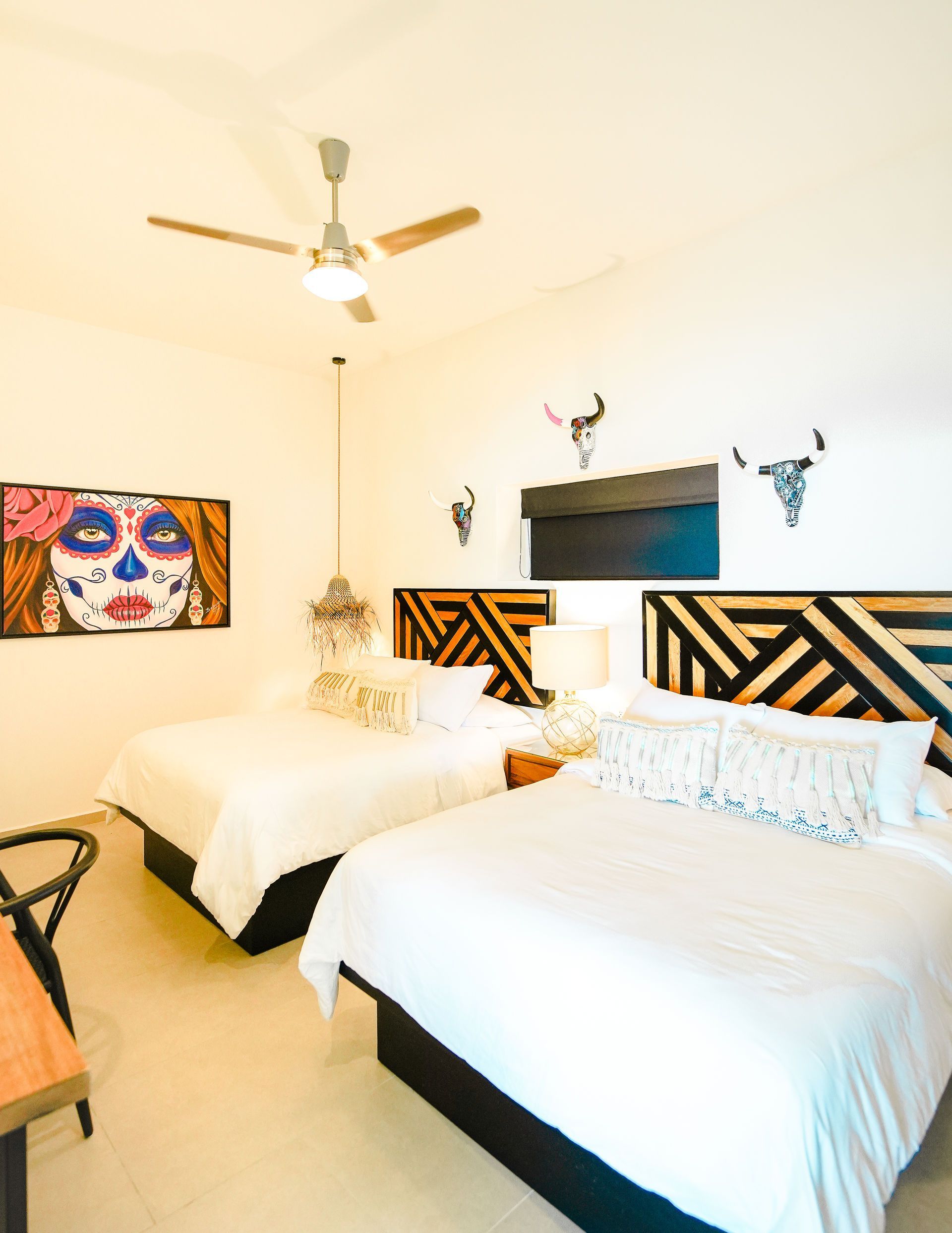 Bright bedroom with two beds, bold black-and-white headboards, wall art, and a ceiling fan.