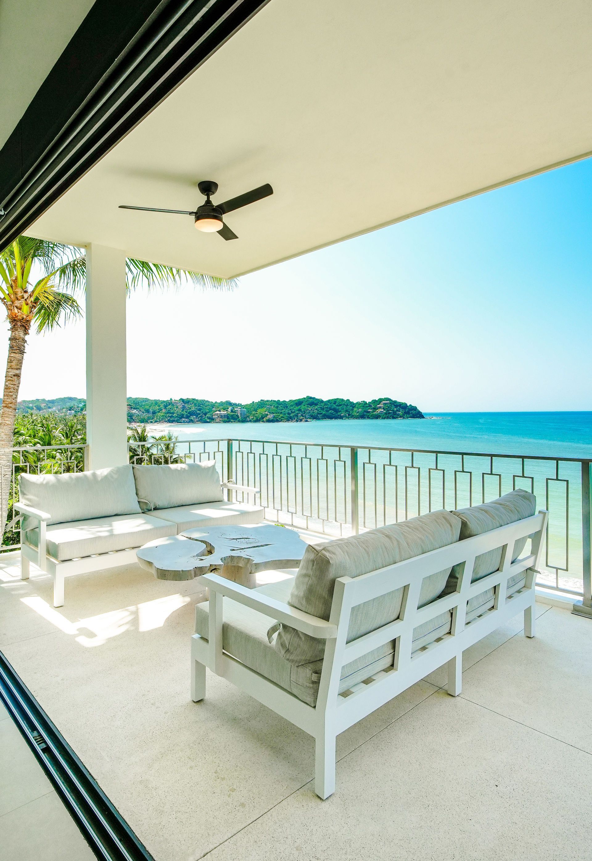 White patio seating overlooking a sunny turquoise ocean and distant shoreline