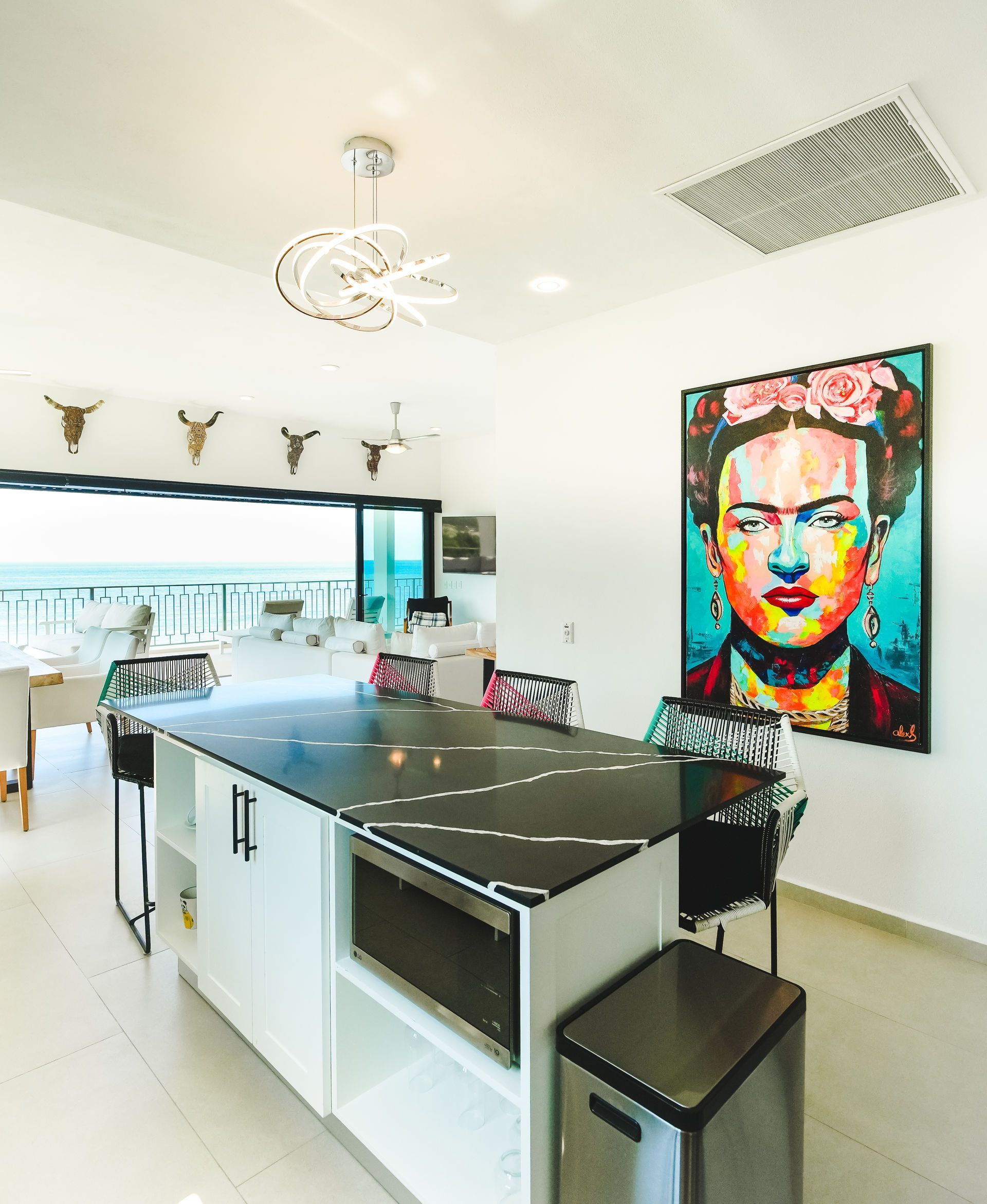 Bright modern kitchen with island, black stools, and colorful portrait artwork on the wall