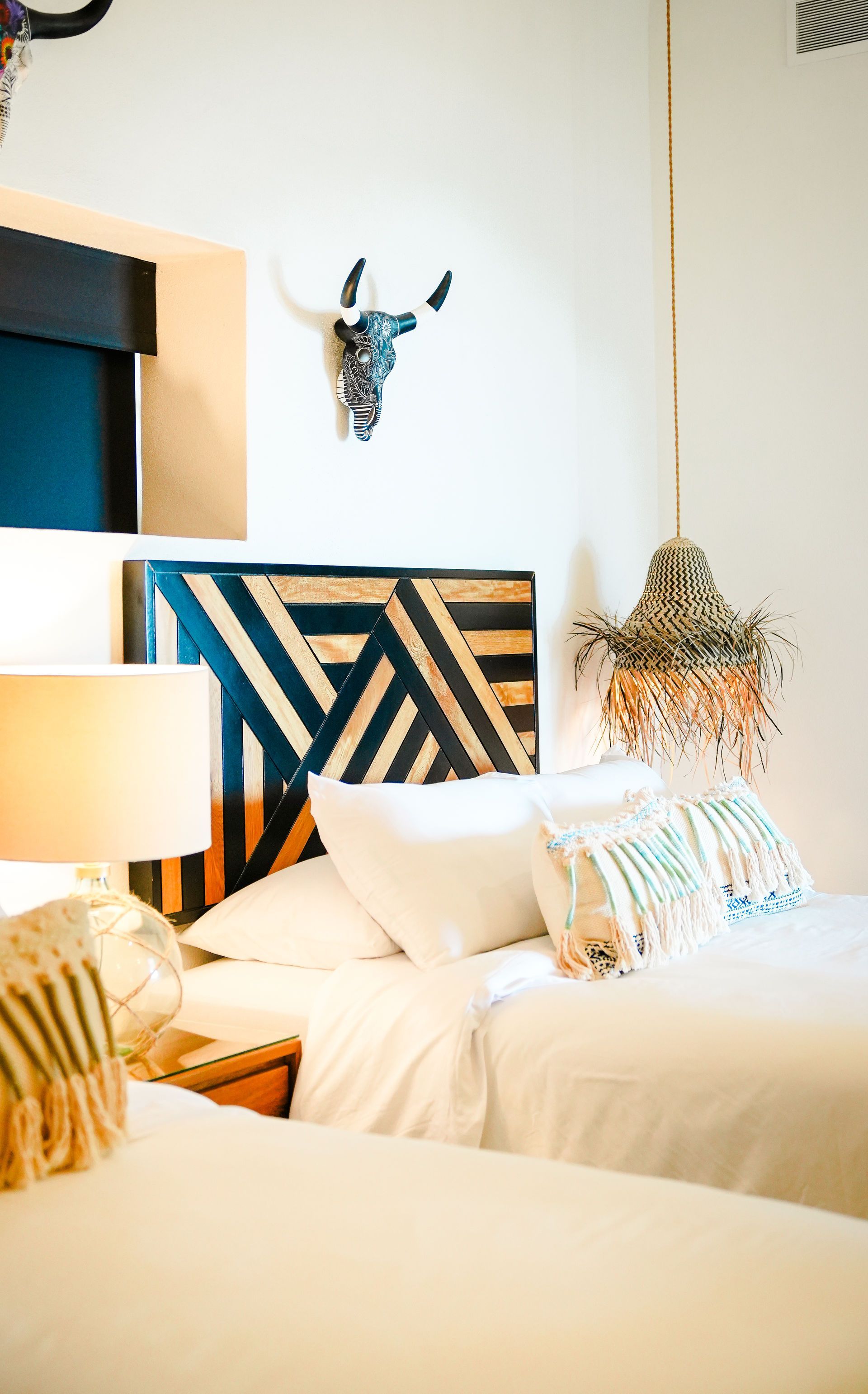 Bright bedroom with a bed, patterned headboard, lamp, and woven wall decor