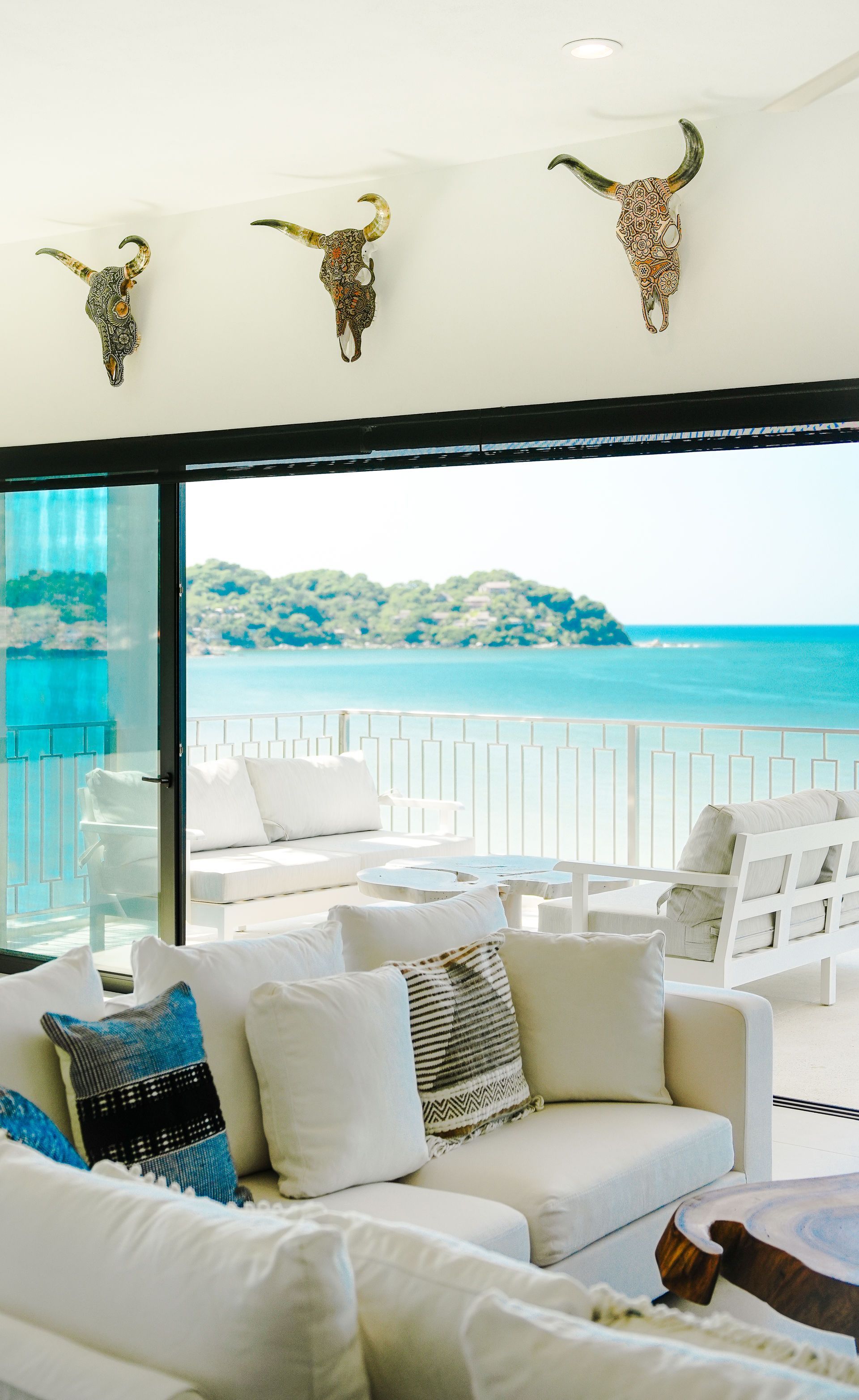 Bright seaside lounge with white sofas, black pillows, and a view of turquoise water and distant islands