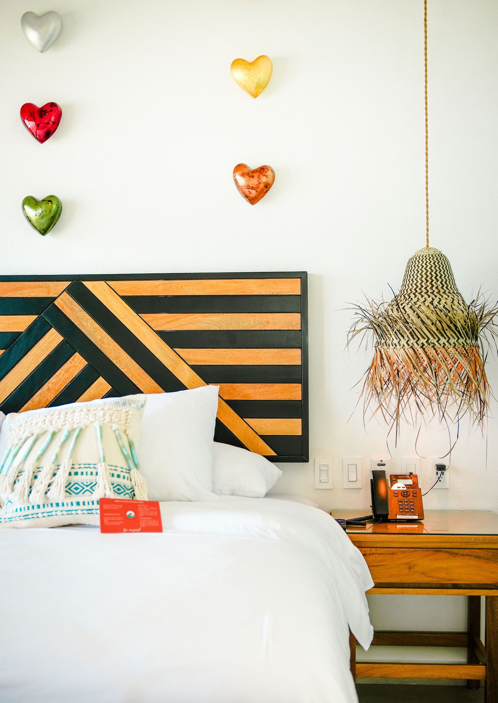 Colorful bedroom with striped headboard, white bed, heart wall decor, and hanging plant by a wooden nightstand
