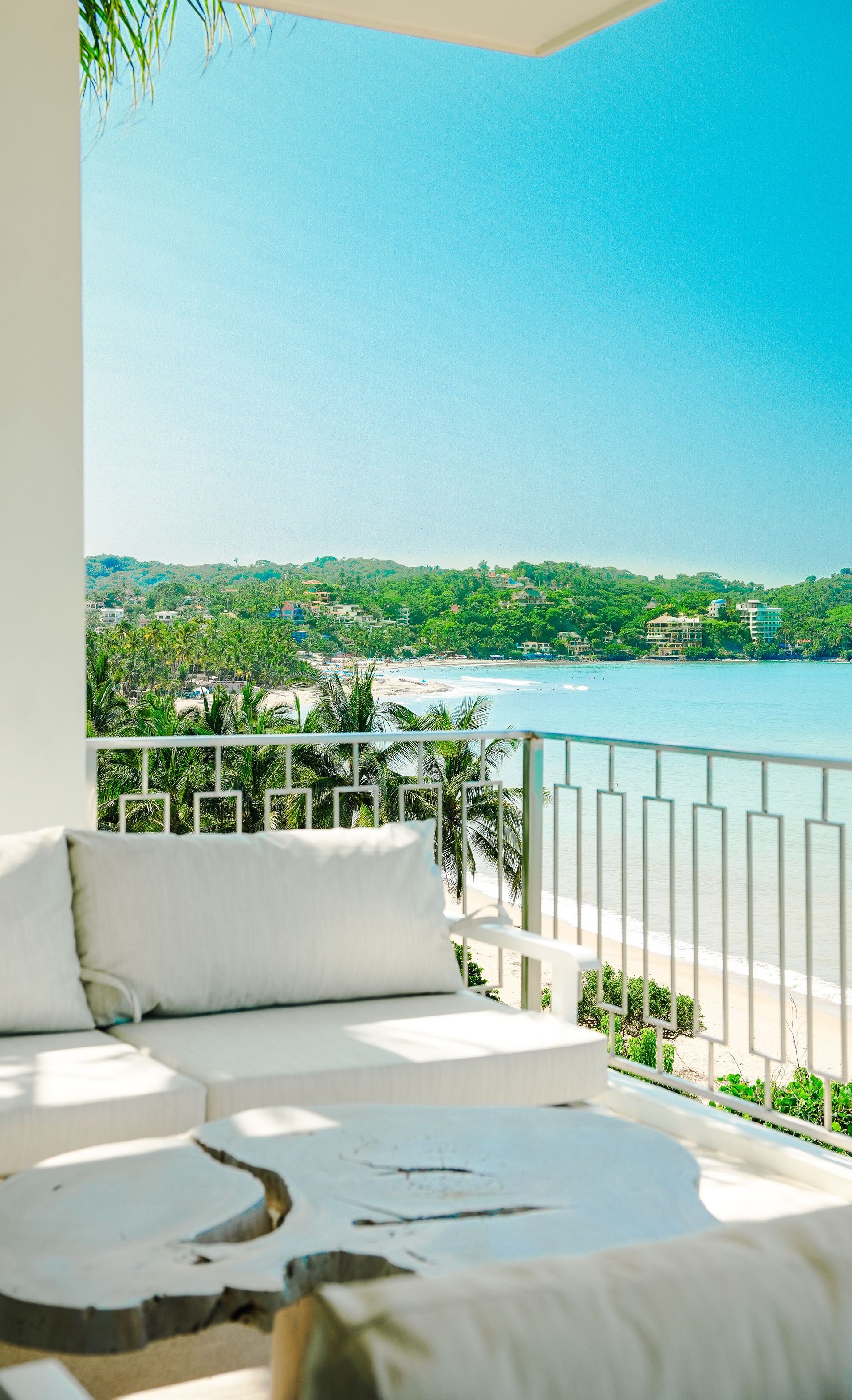White patio seating overlooking a calm blue waterfront and green shoreline under a bright sky