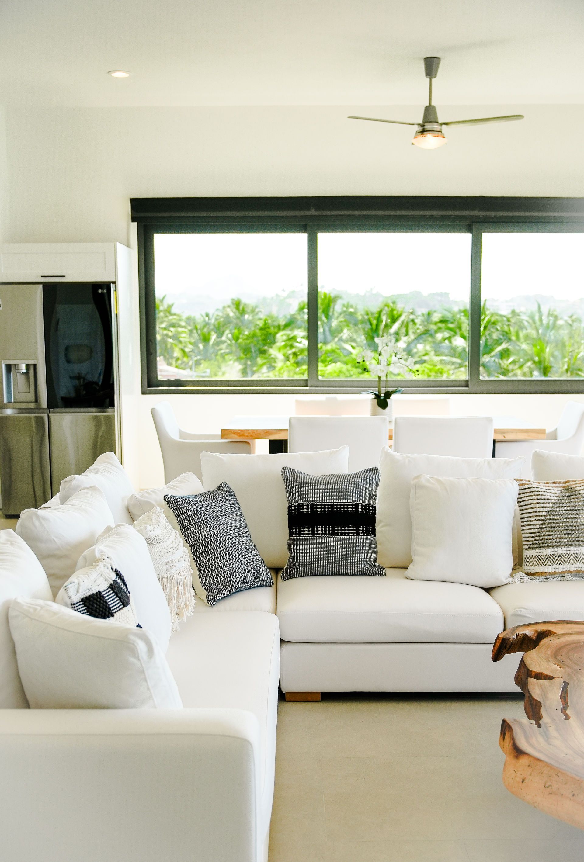 Bright living room with white sectional sofa, patterned pillows, large window, and ceiling fan
