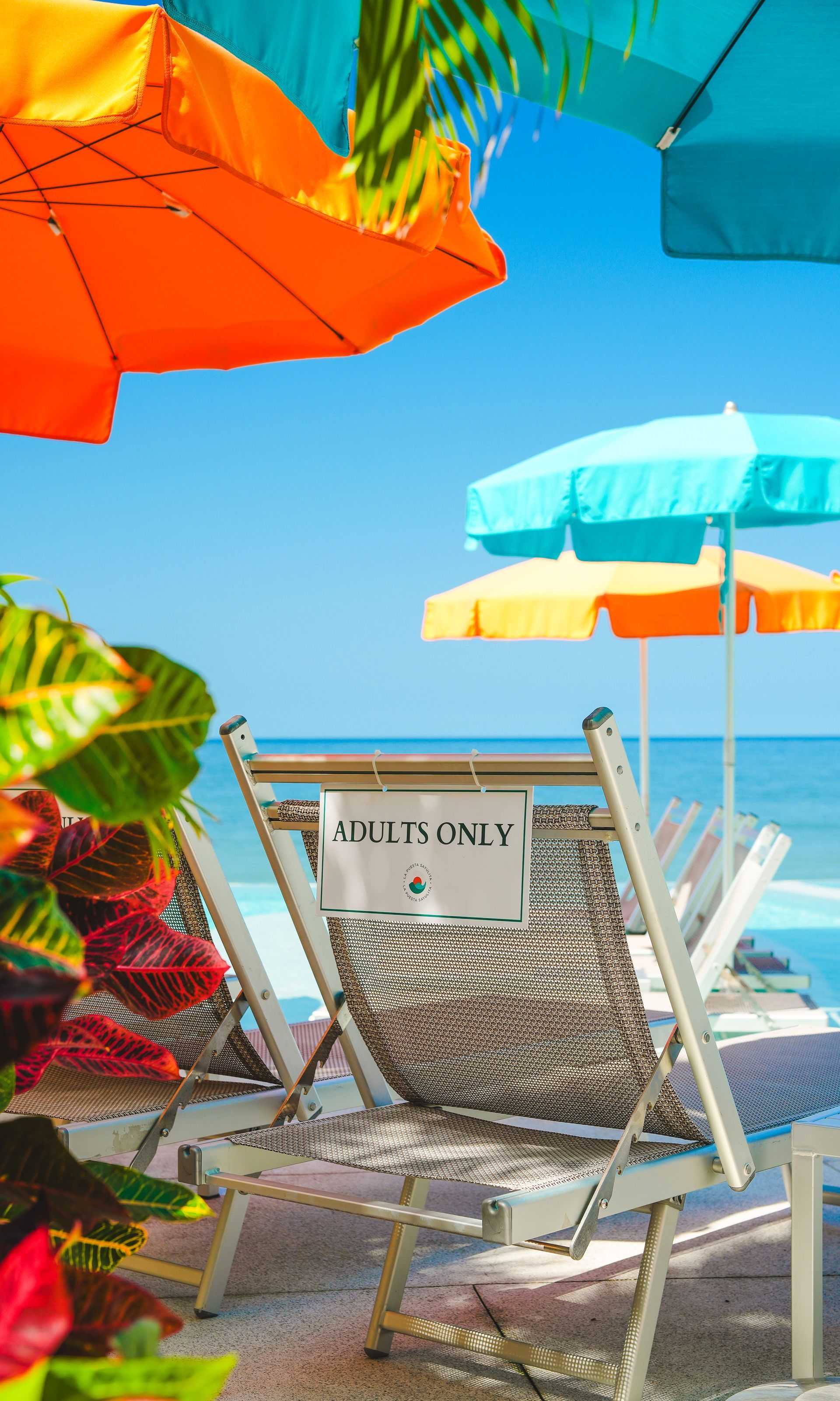 Beach chair under colorful umbrellas with a “Guests Only” sign by the shore