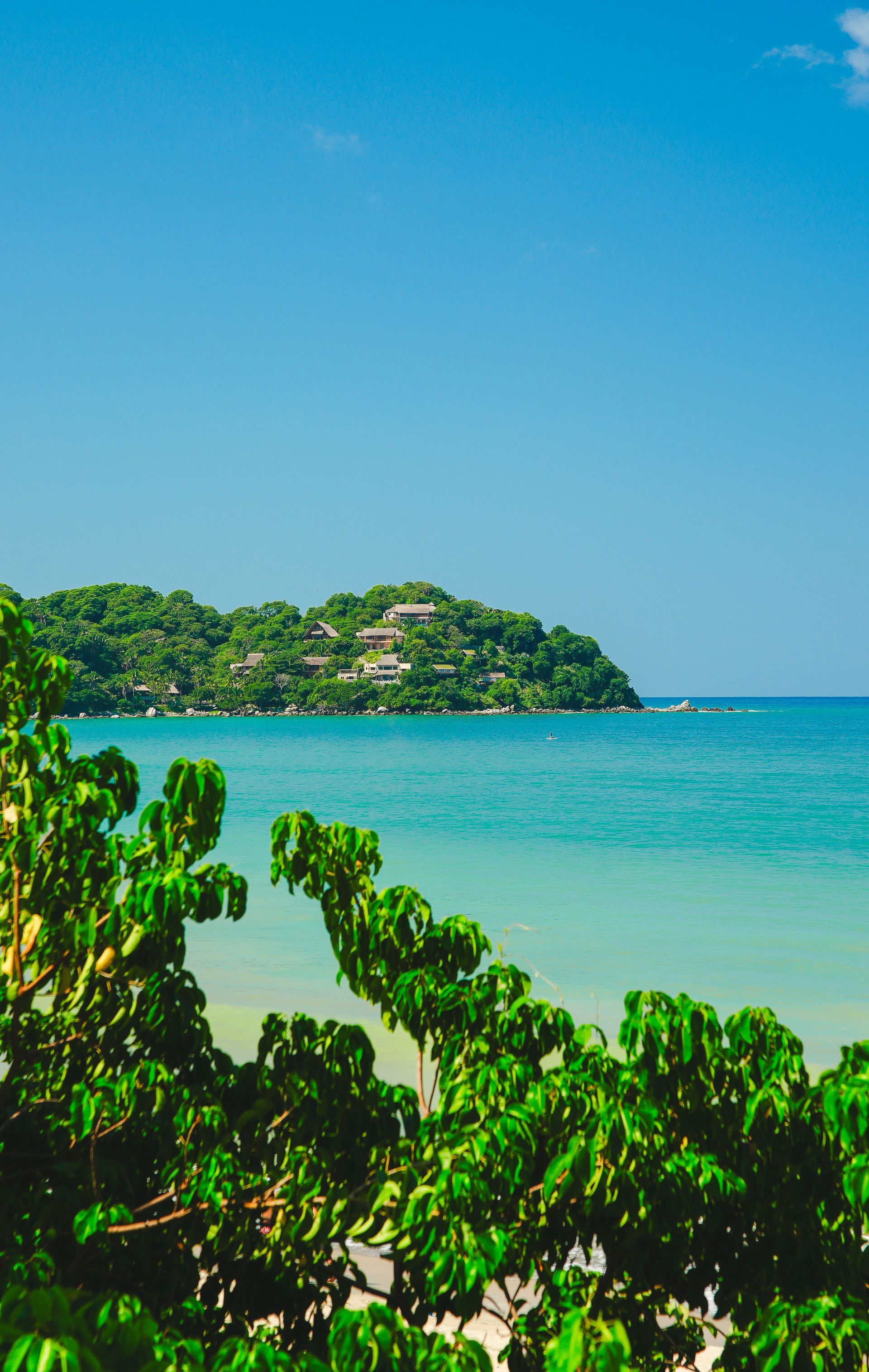 Tropical beach with turquoise water, green shoreline, and a small island under a clear blue sky