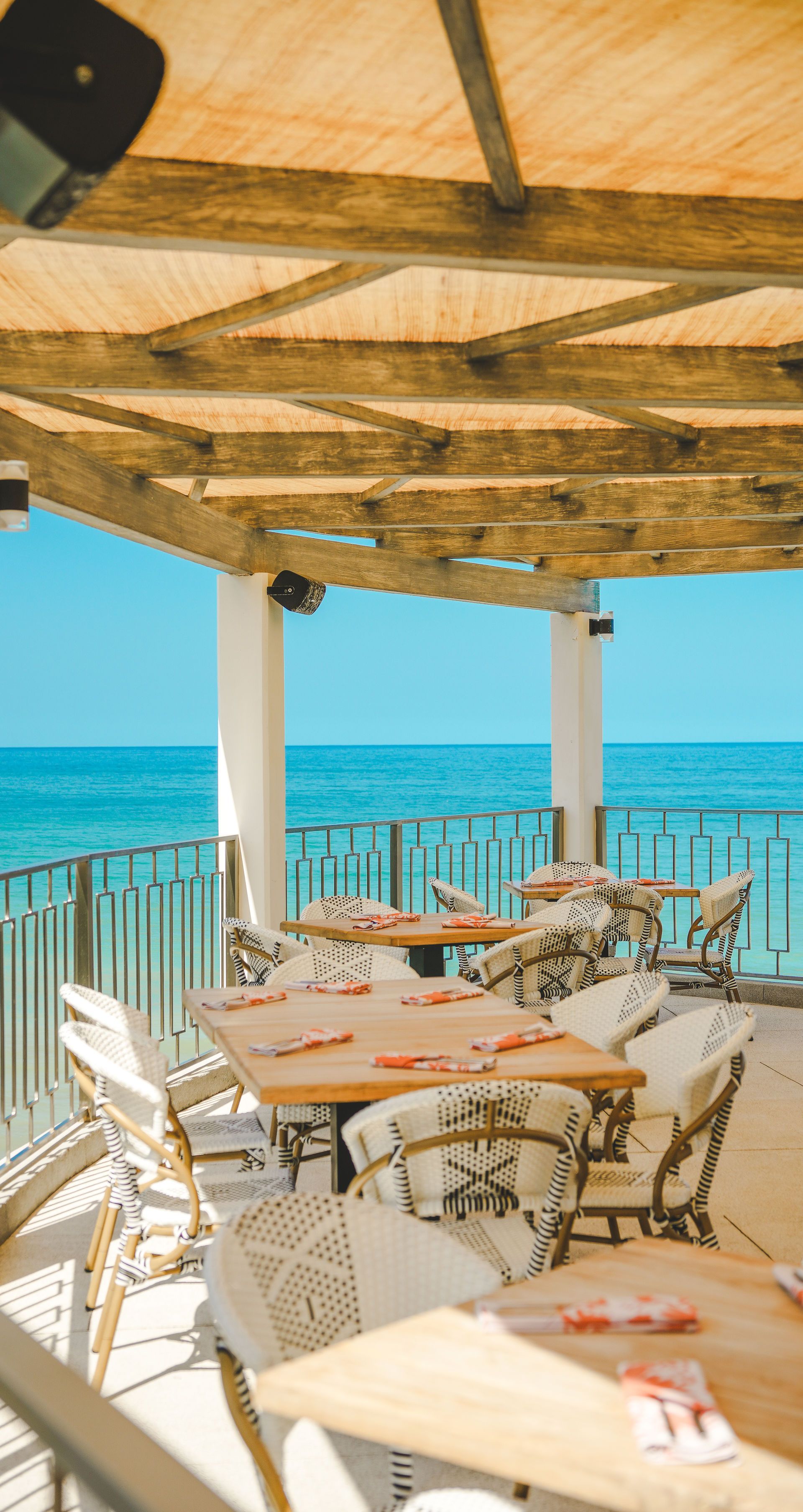 Seaside café terrace with wooden pergola, tables, chairs, and ocean view