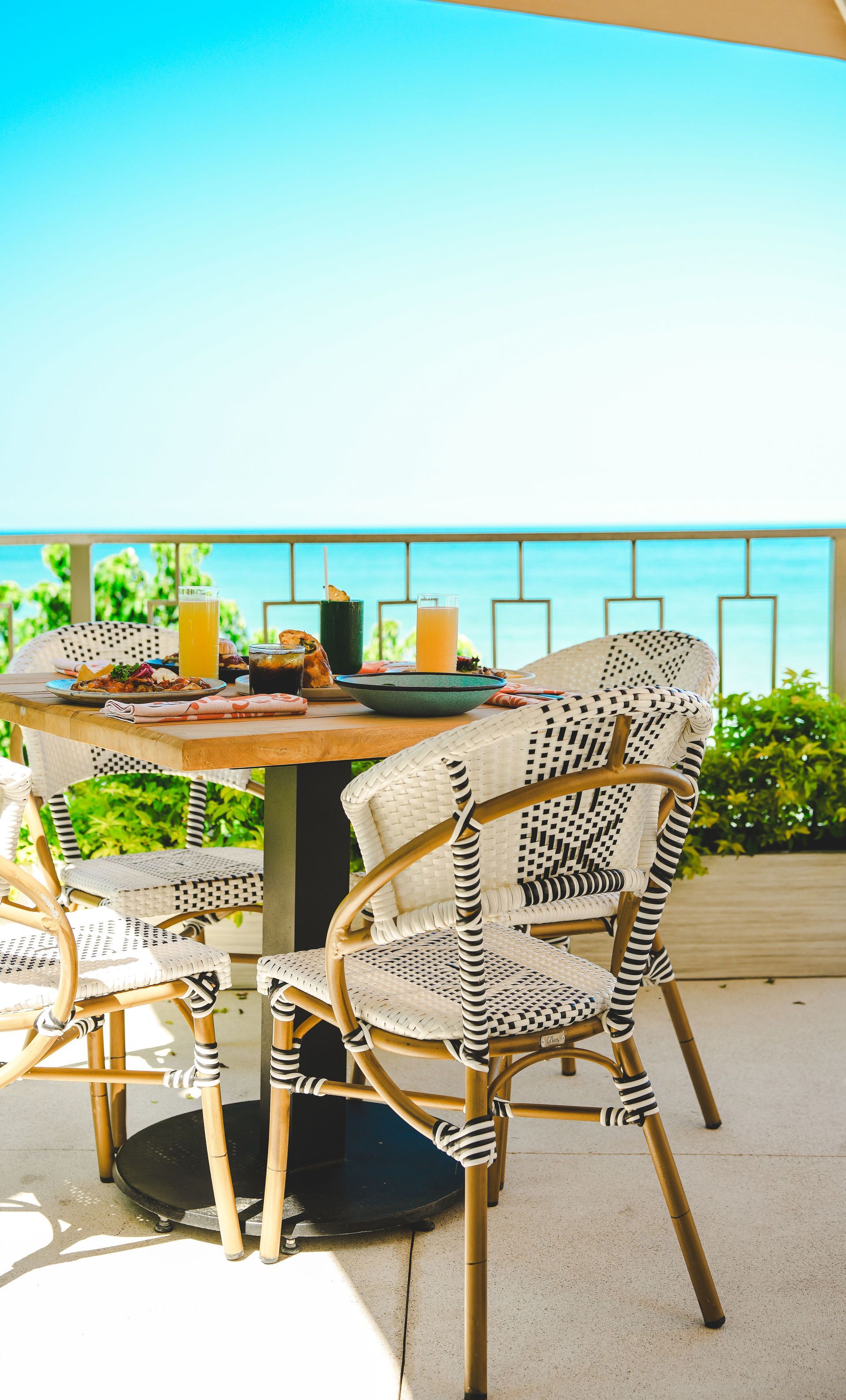 Outdoor patio with wicker chairs and a dining table overlooking the ocean under a blue canopy