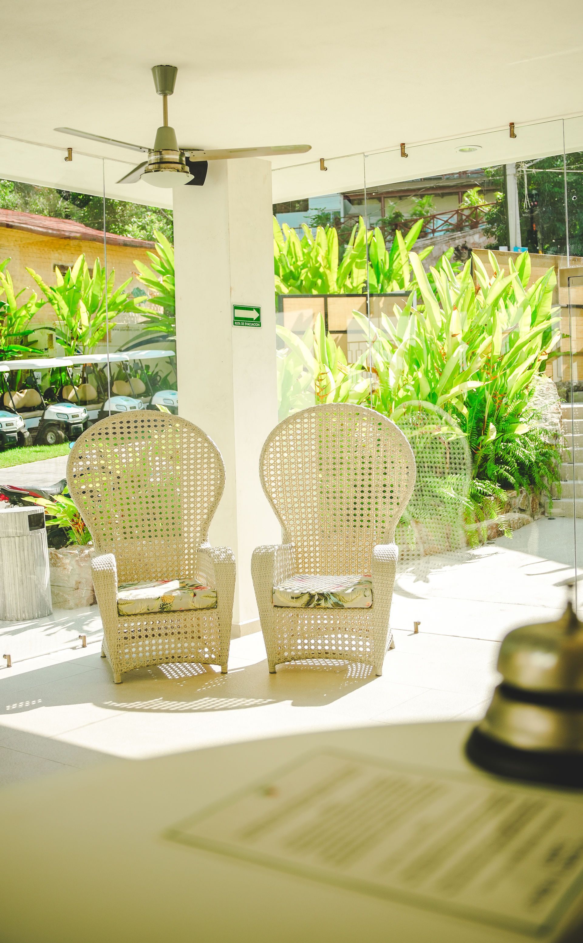 Two wicker chairs on a bright patio with tropical plants and a ceiling fan overhead.