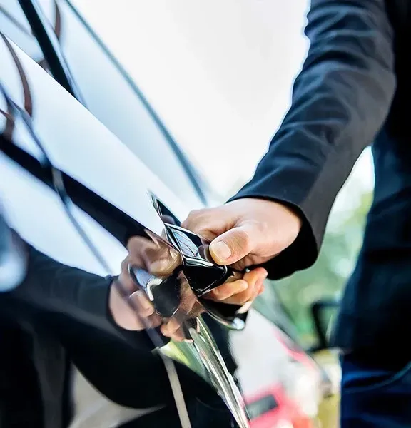 A person plugs a charging cable into a black car’s side port outdoors.