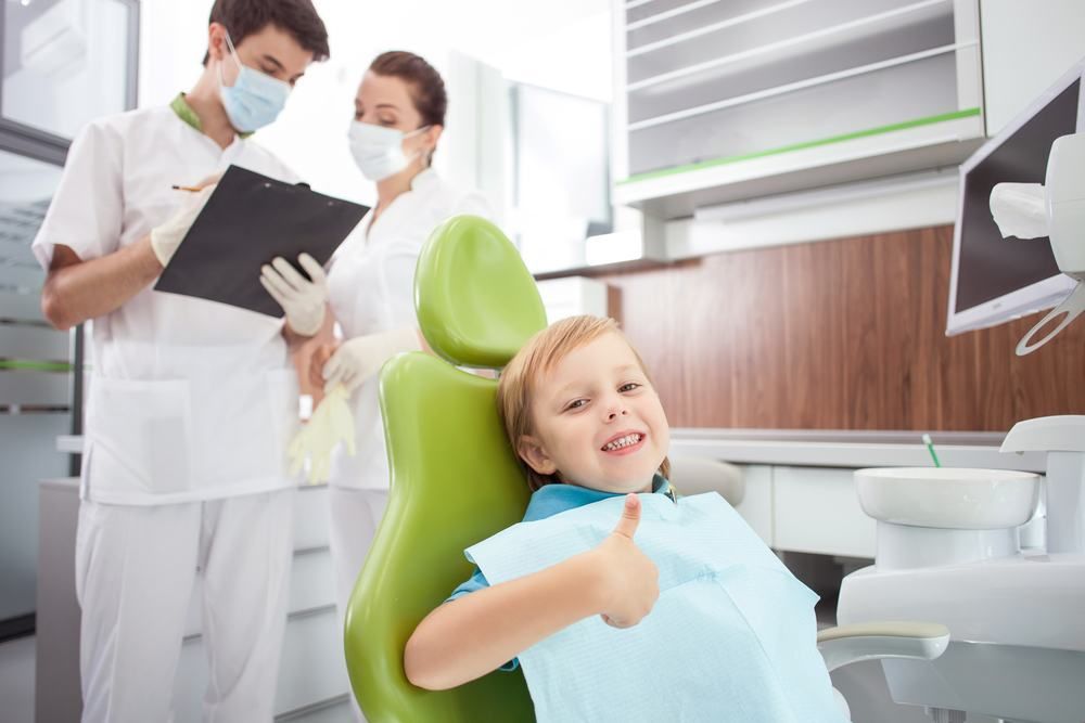 A Young Boy Is Sitting In A Dental Chair Giving A Thumbs Up — Dental Care Smithfield In Smithfield, QLD