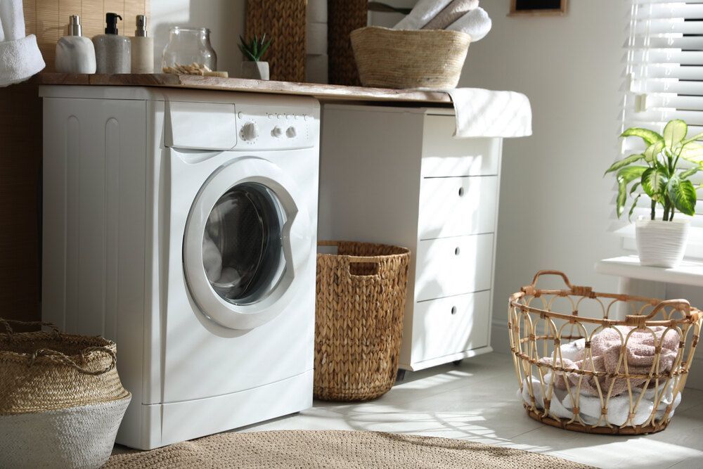 A Laundry Room With a Washing Machine and a Basket of Towels — Bruce Smith Cabinets in Tweed Heads, NSW