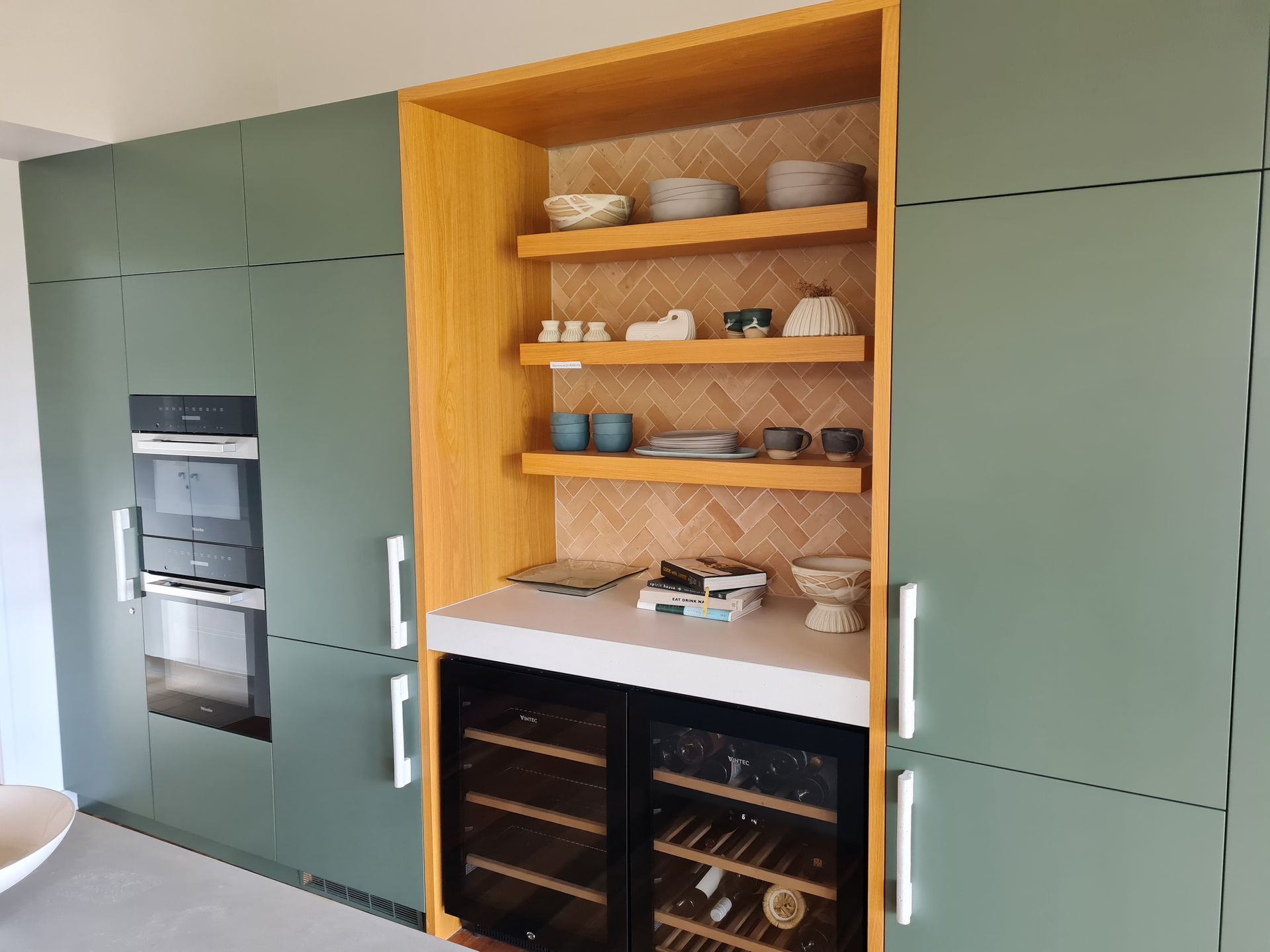 A kitchen with green cabinets and a wine cooler.